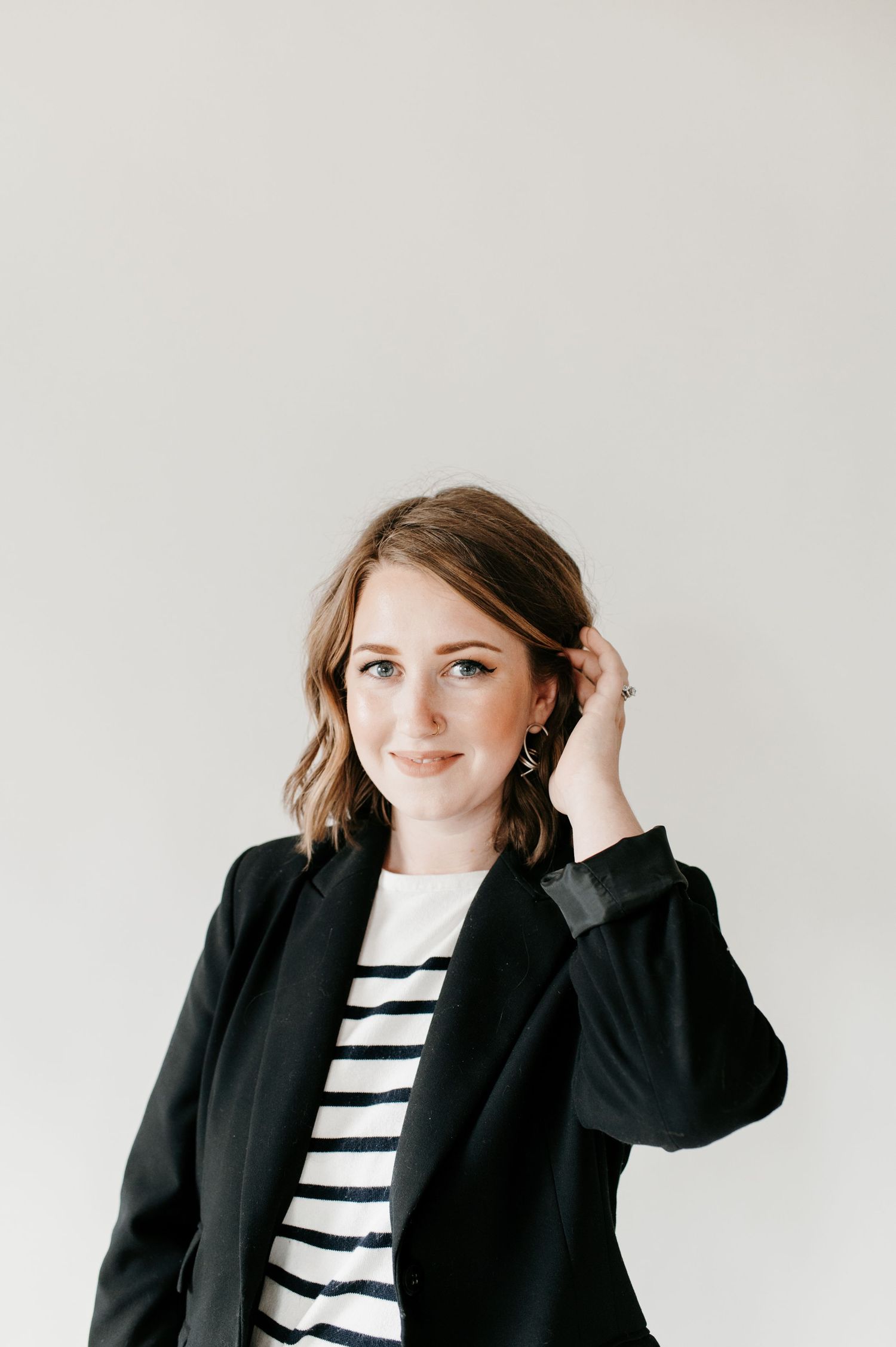 Professional lifestyle portrait showing figure in black blazer and striped shirt against light background.
