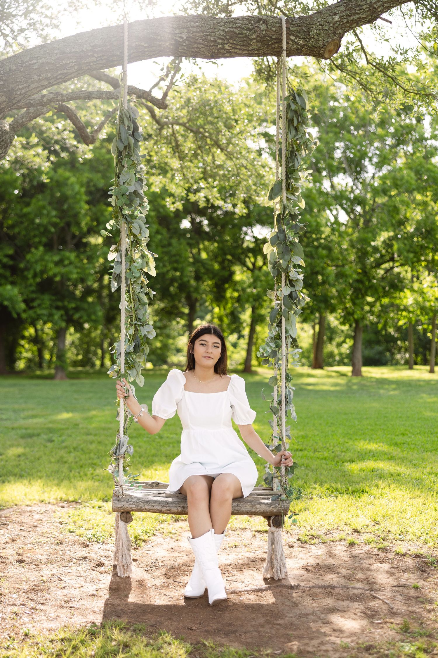 A wooden swing adorned with delicate vines hangs from a tree branch in a sunlit summer garden.