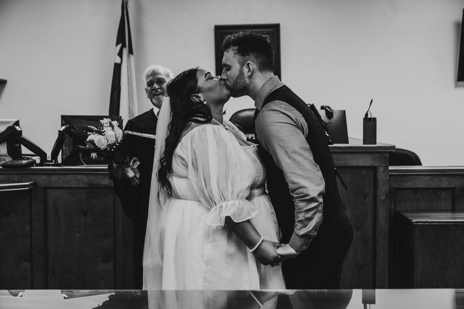 A couple shares a tender kiss during an intimate courthouse wedding ceremony in black and white photography.