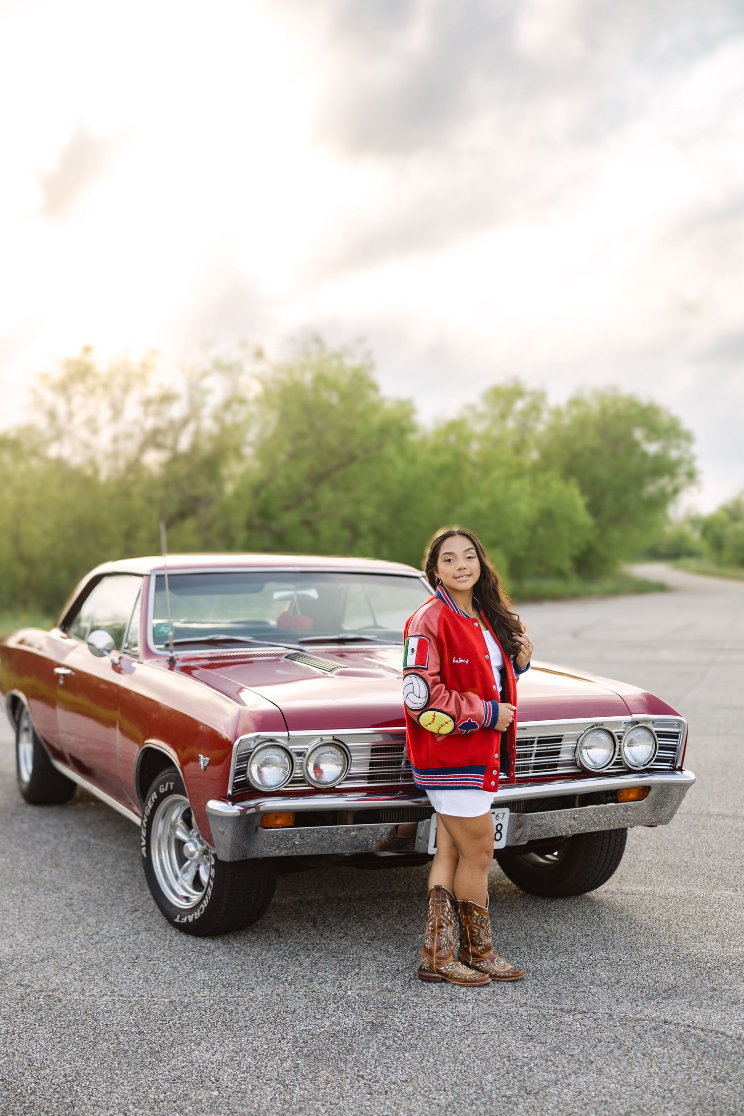 Classic maroon 1967 Chevrolet Chevelle SS muscle car parked on road with trees and cloudy sky in background.