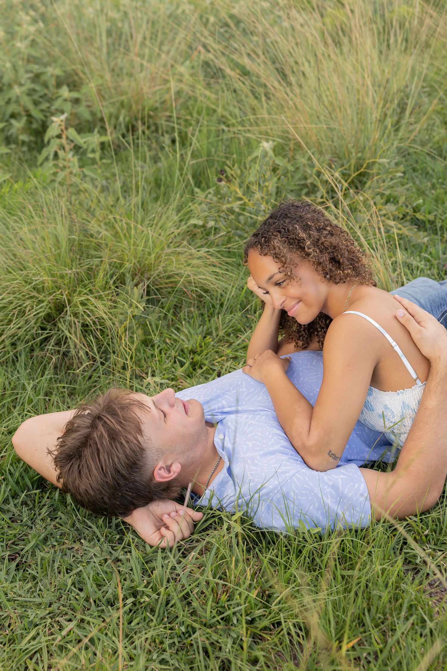 Young couple lying together in tall grass on a sunny day sharing an intimate moment outdoors.
