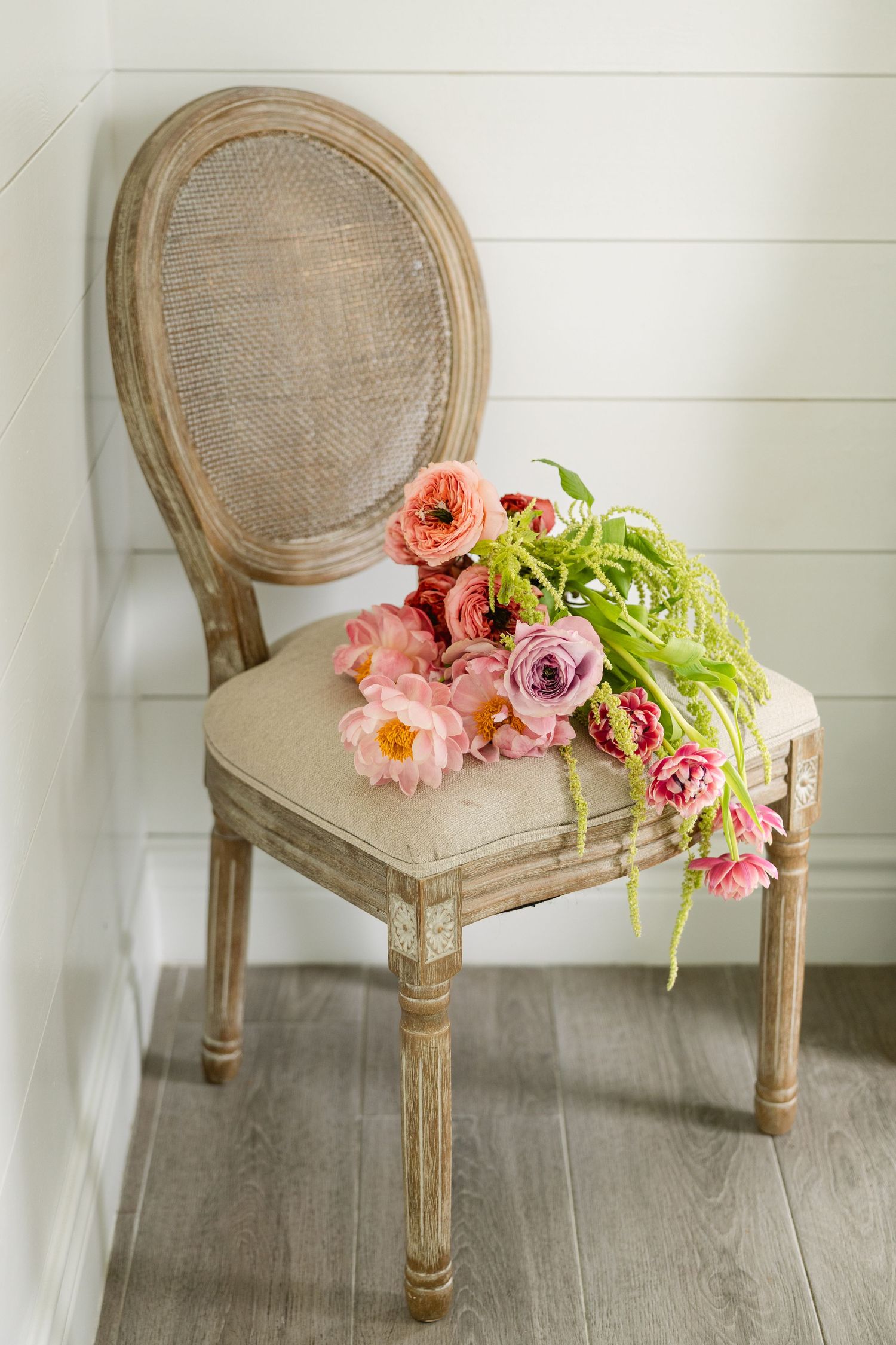 Beautiful pink roses and flowers arranged on a vintage French cane back dining chair with whitewashed finish.