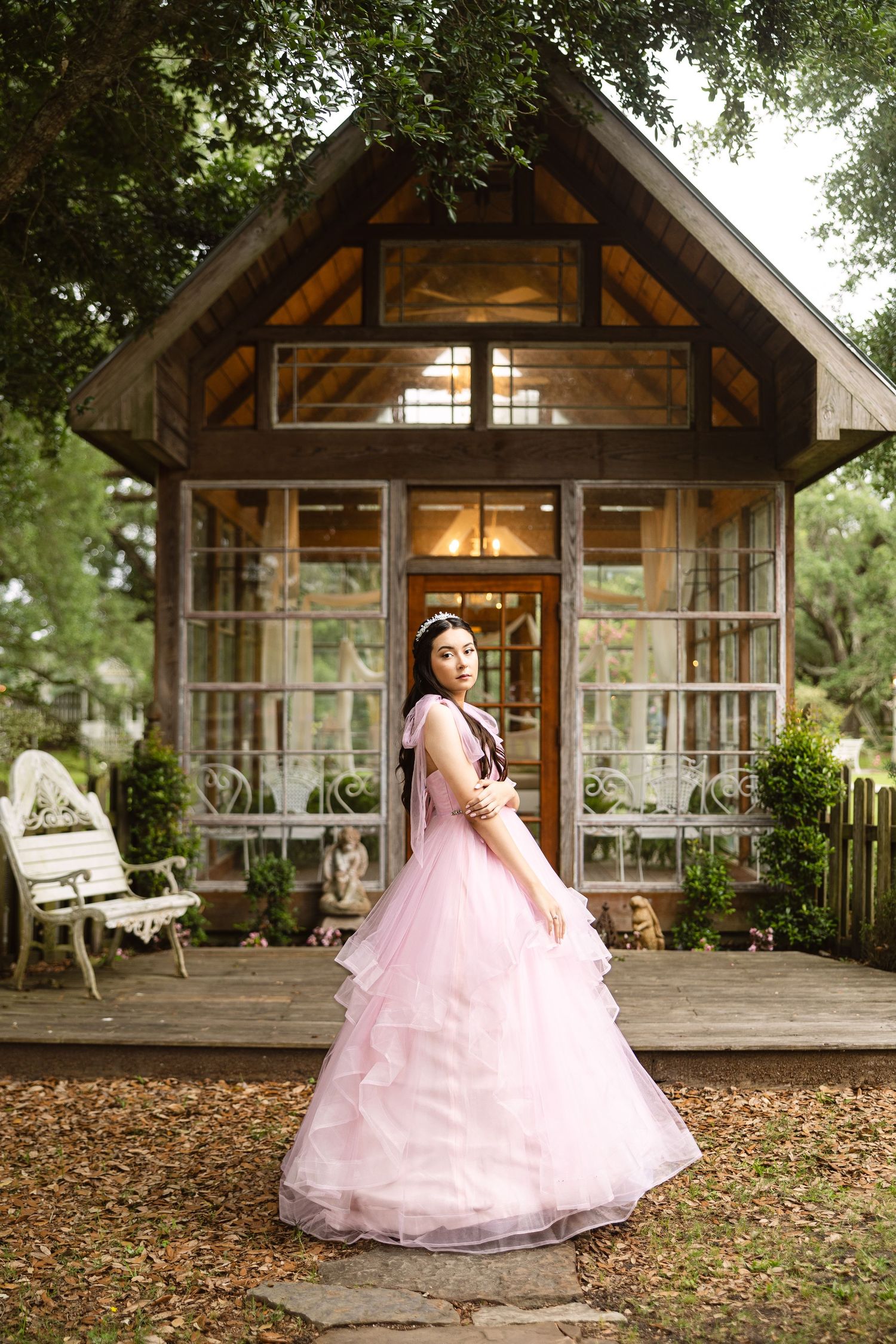 A pink tulle ballgown in front of a rustic glass cabin with warm lighting and wooden beams.