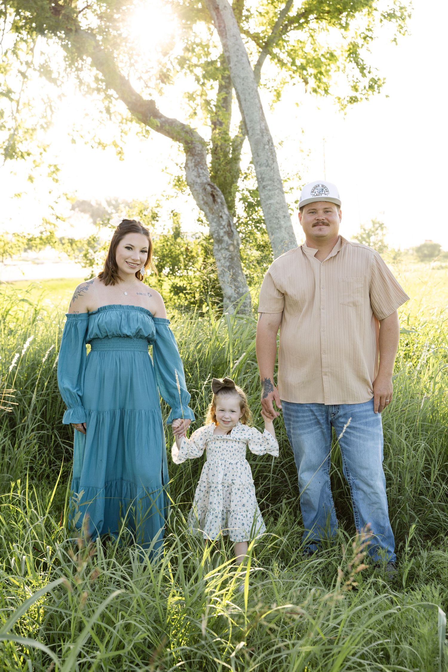 Scenic outdoor family photo session in tall grass field during golden hour with soft natural lighting.