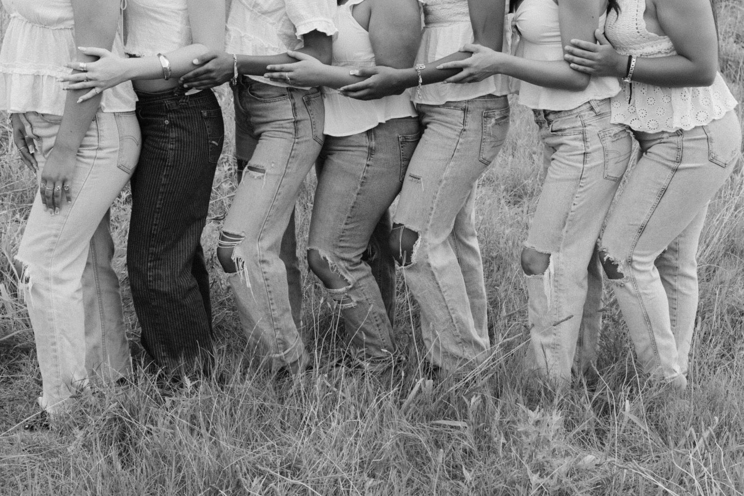 A row of people wearing khaki pants and light colored shirts stand informally together outdoors.