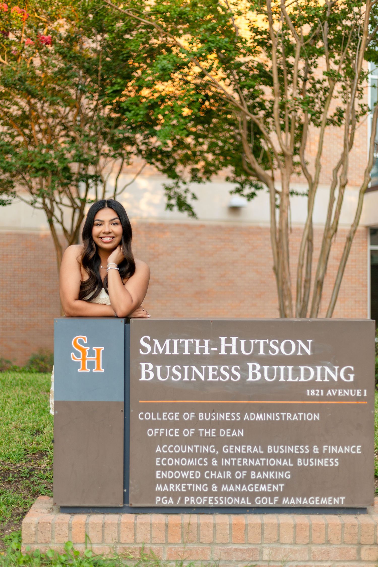 Outdoor view of the Smith-Hutson Business Building sign with trees and landscaping on a college campus.