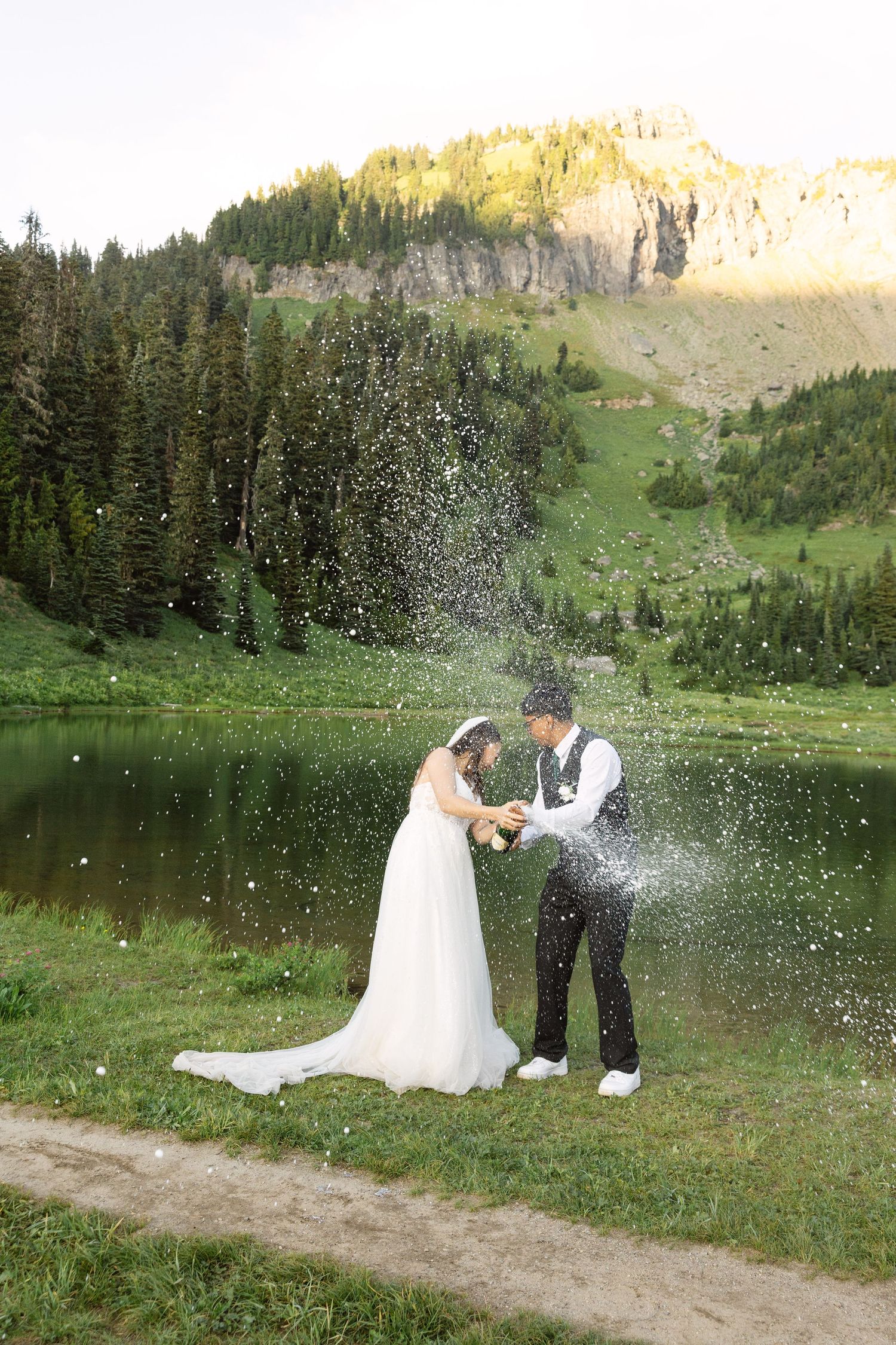A couple playfully splashes water at each other during their wedding photoshoot in a scenic mountain landscape.