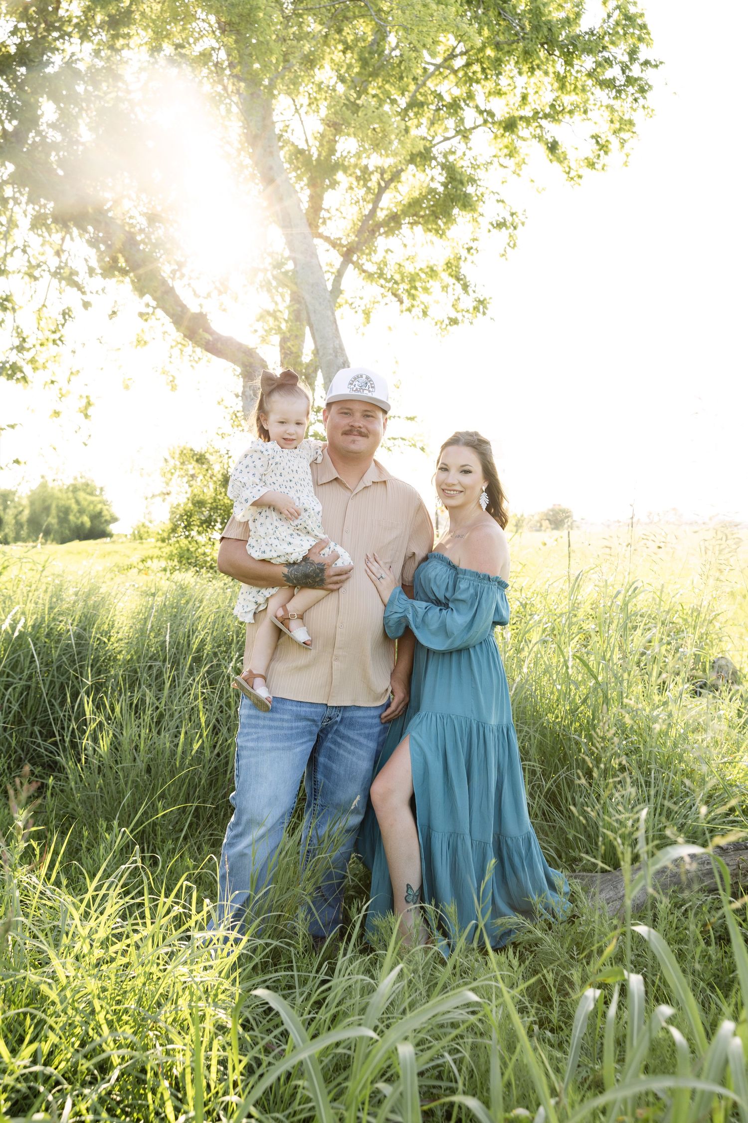 Family enjoying a tender outdoor moment together in a sunlit field of tall grass during golden hour.