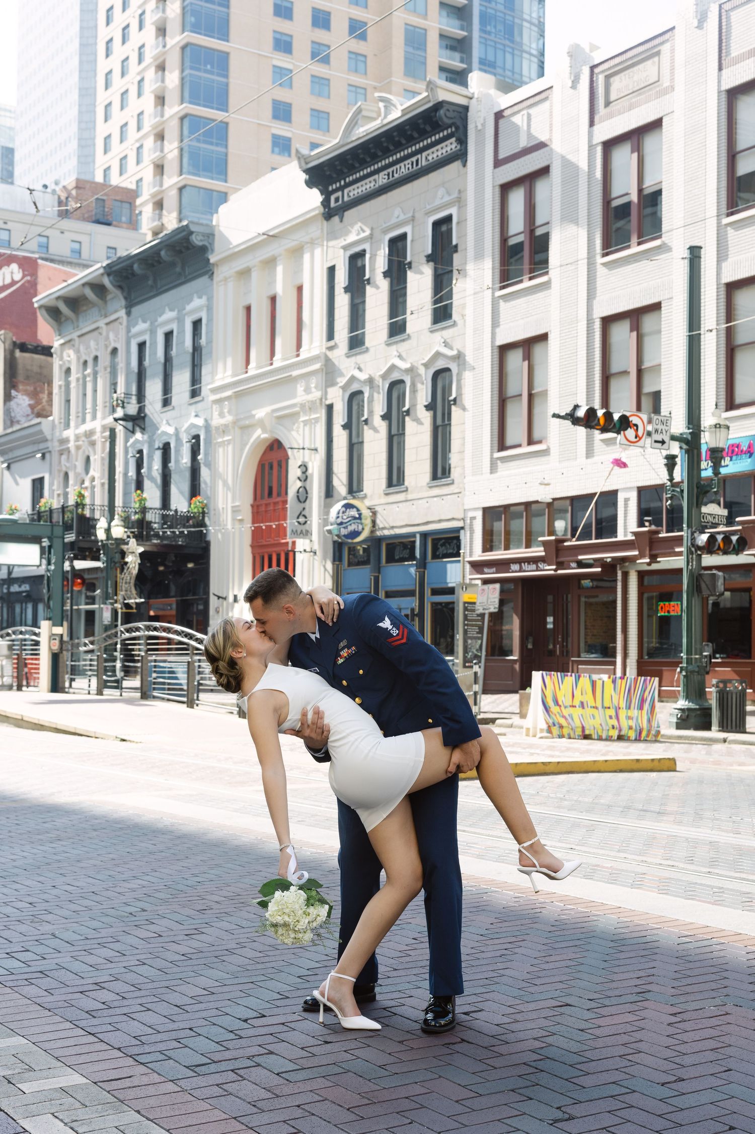 A romantic dance dip captured on a historic brick-lined city street with classic architecture and modern buildings in background.