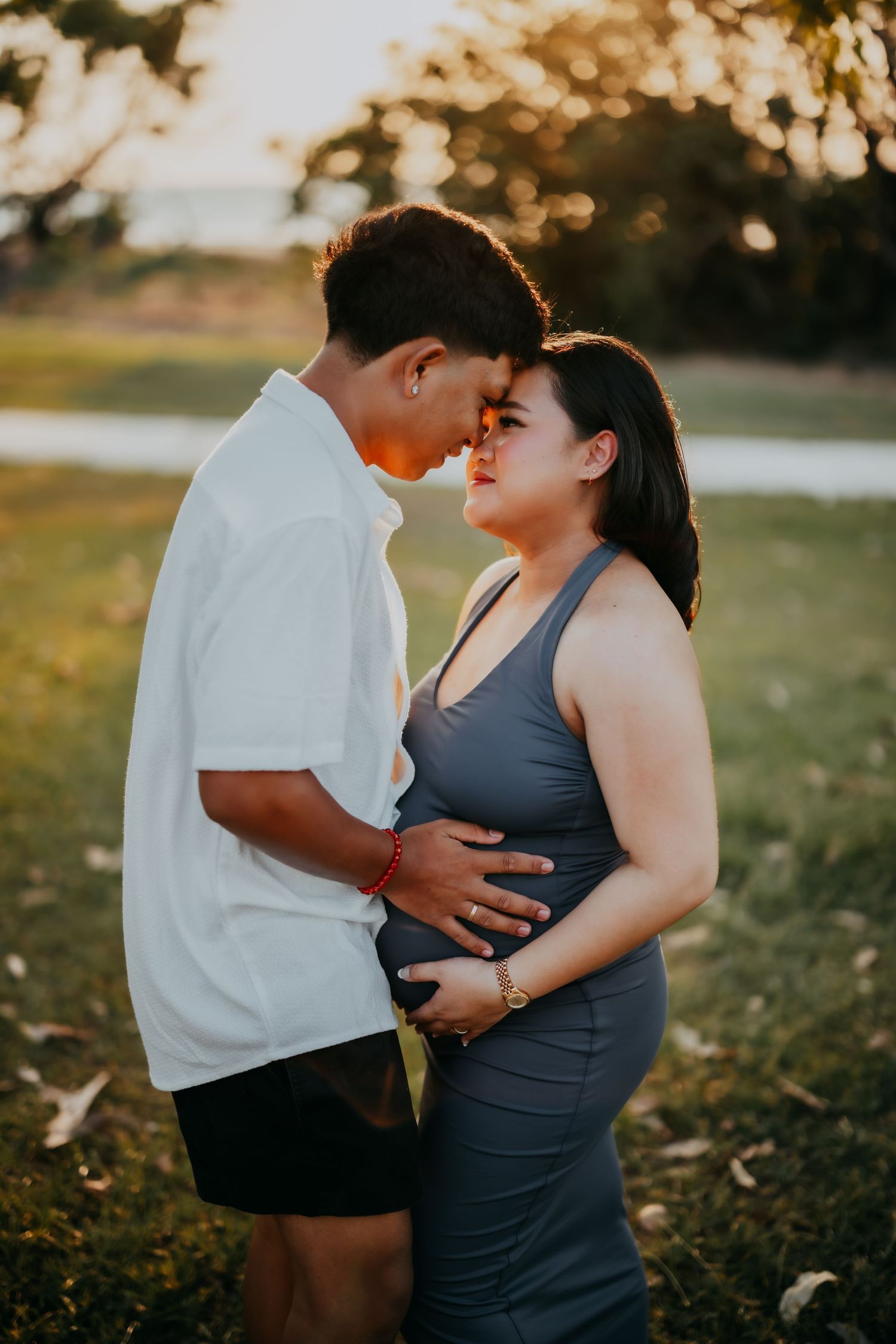 Couple sharing a tender moment, pregnant woman in grey dress with partner at sunset.