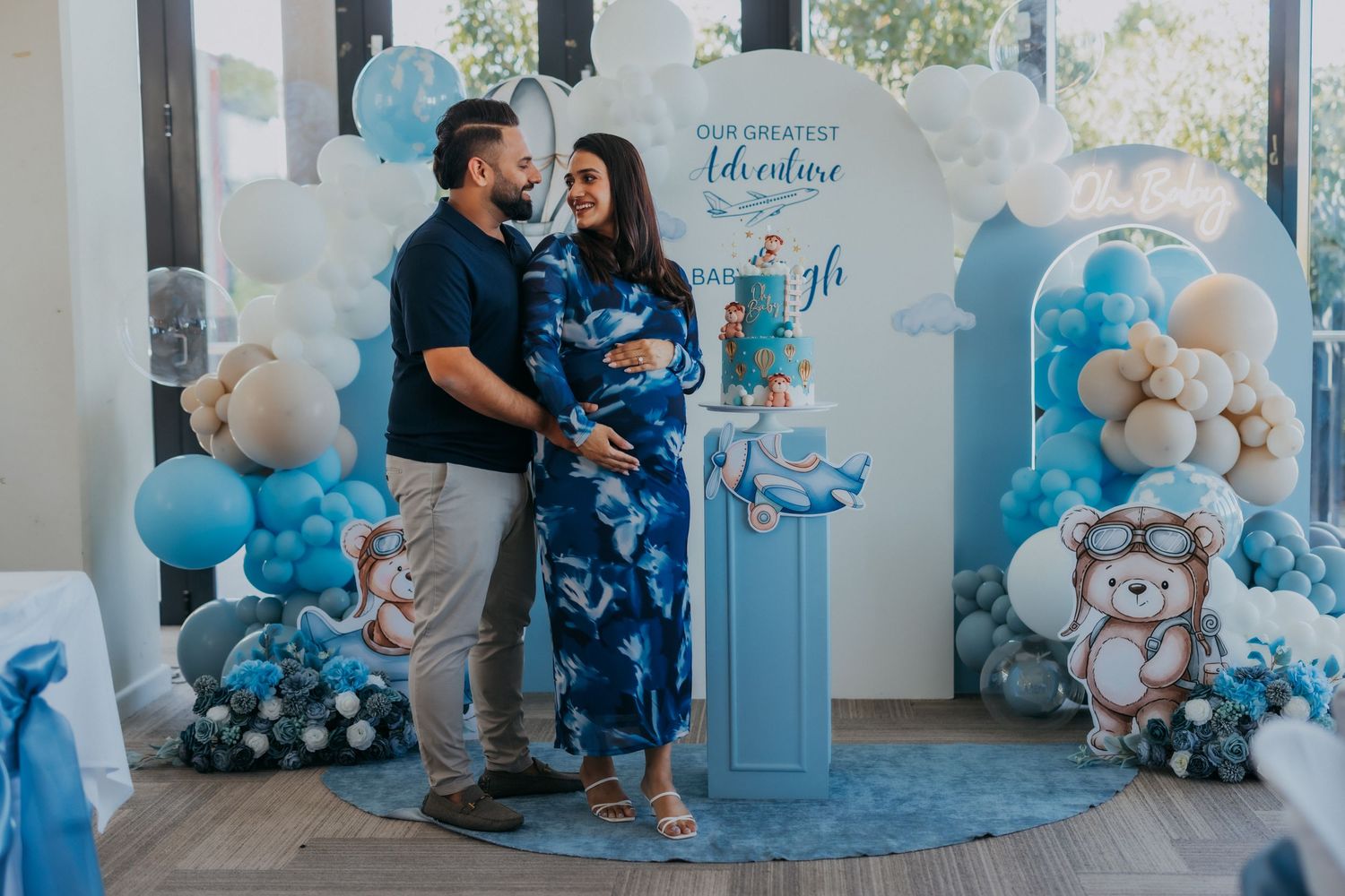 Couple embracing at blue adventure themed baby shower with balloon decorations.