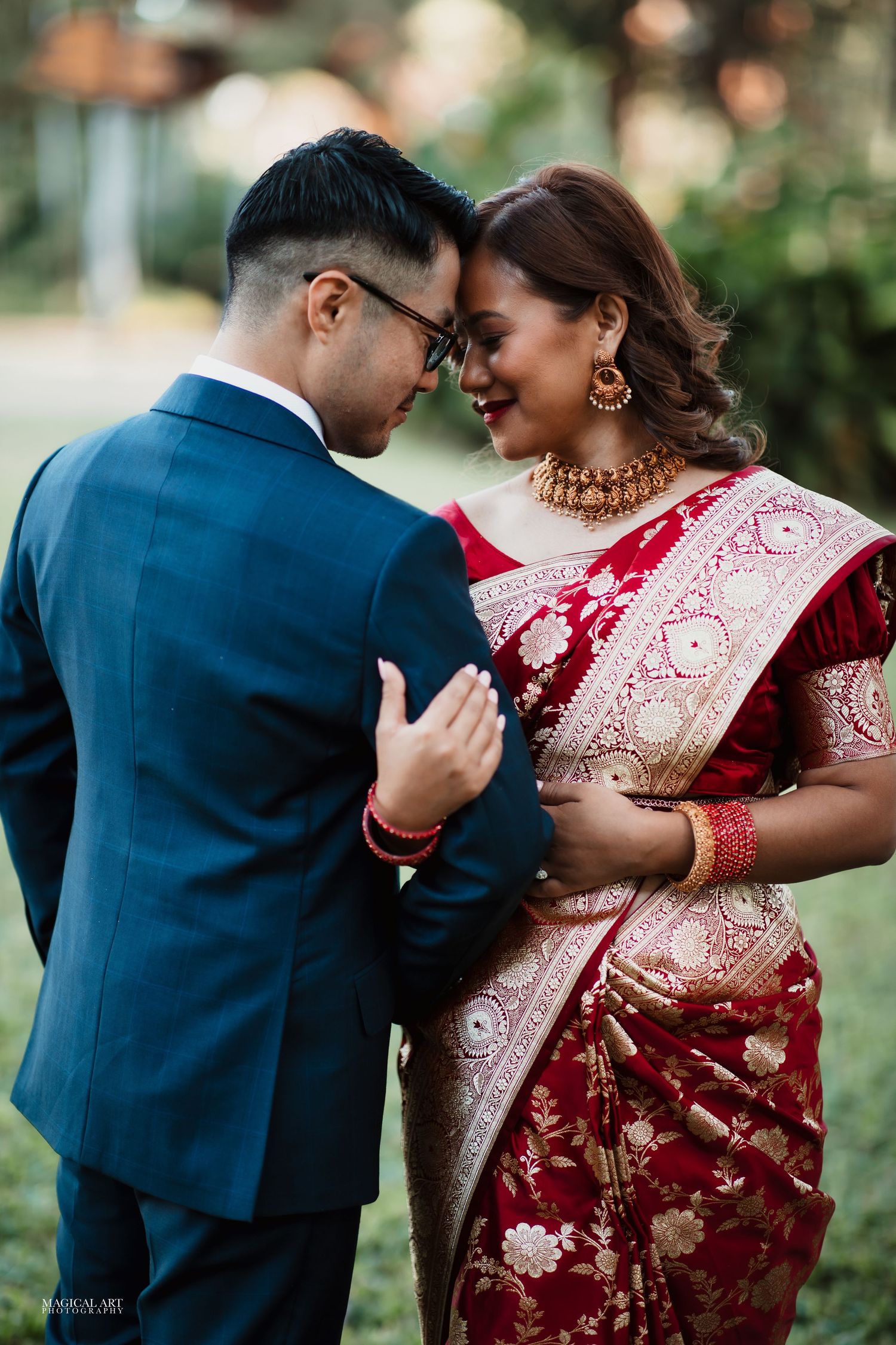 Romantic couple moment with bride in red Banarasi saree and groom in navy suit touching foreheads.