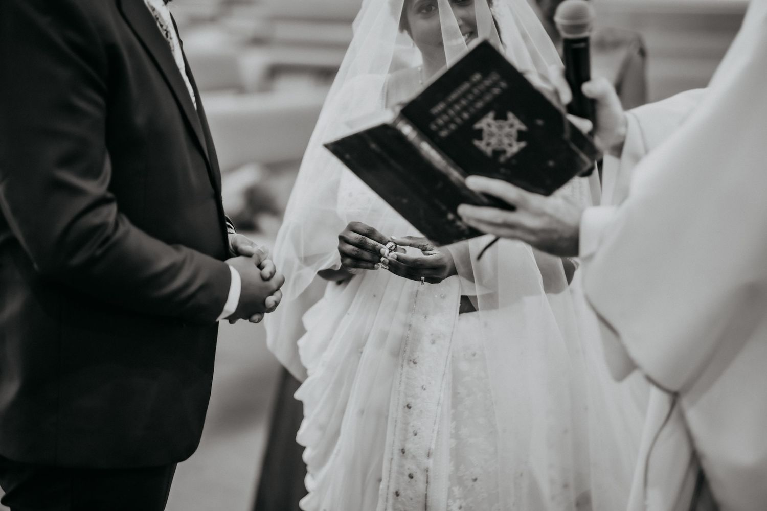 Black and white close-up of wedding ring exchange ceremony with officiant holding Bible.