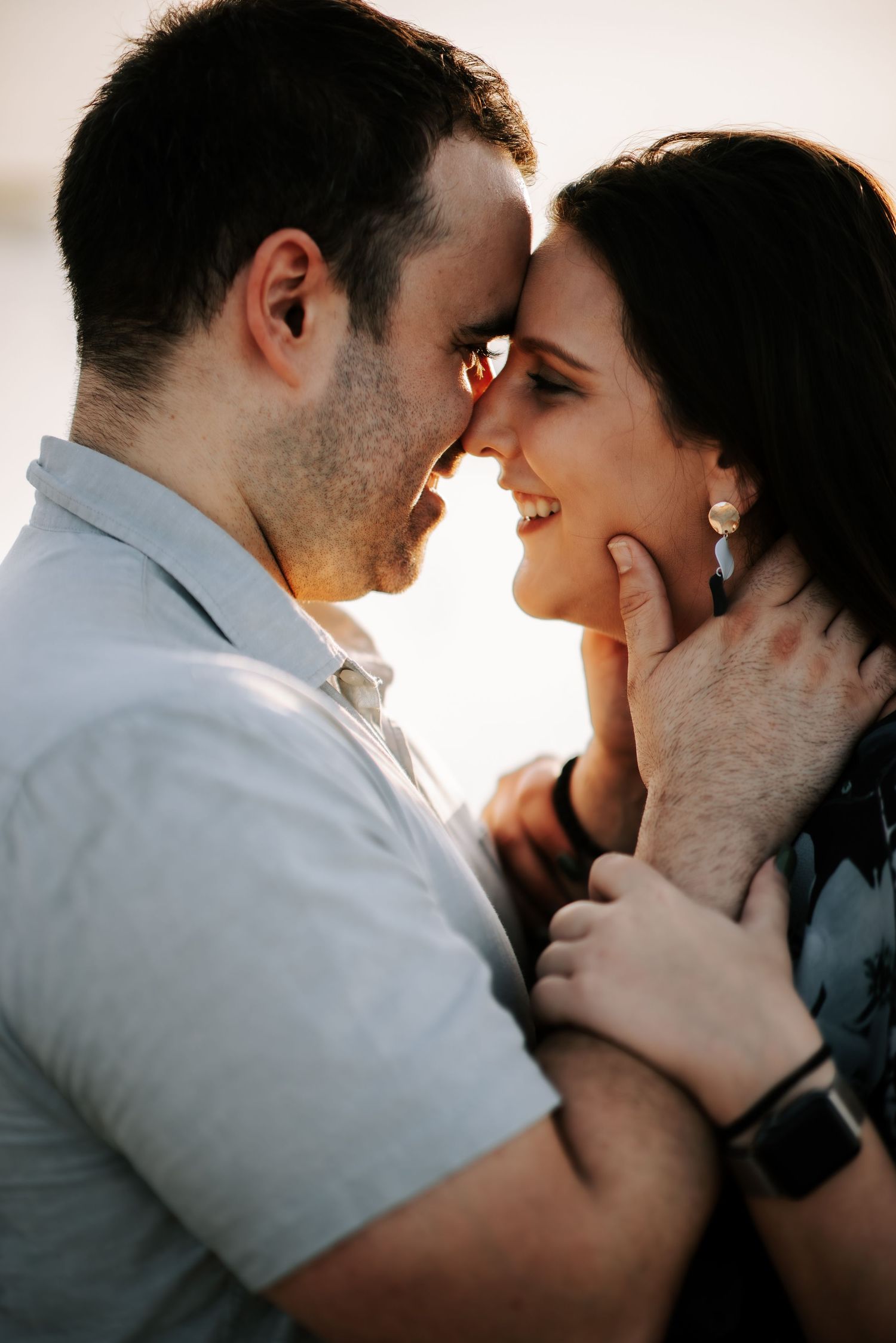 Romantic couple touching foreheads and smiling in warm golden sunset backlight at the beach.
