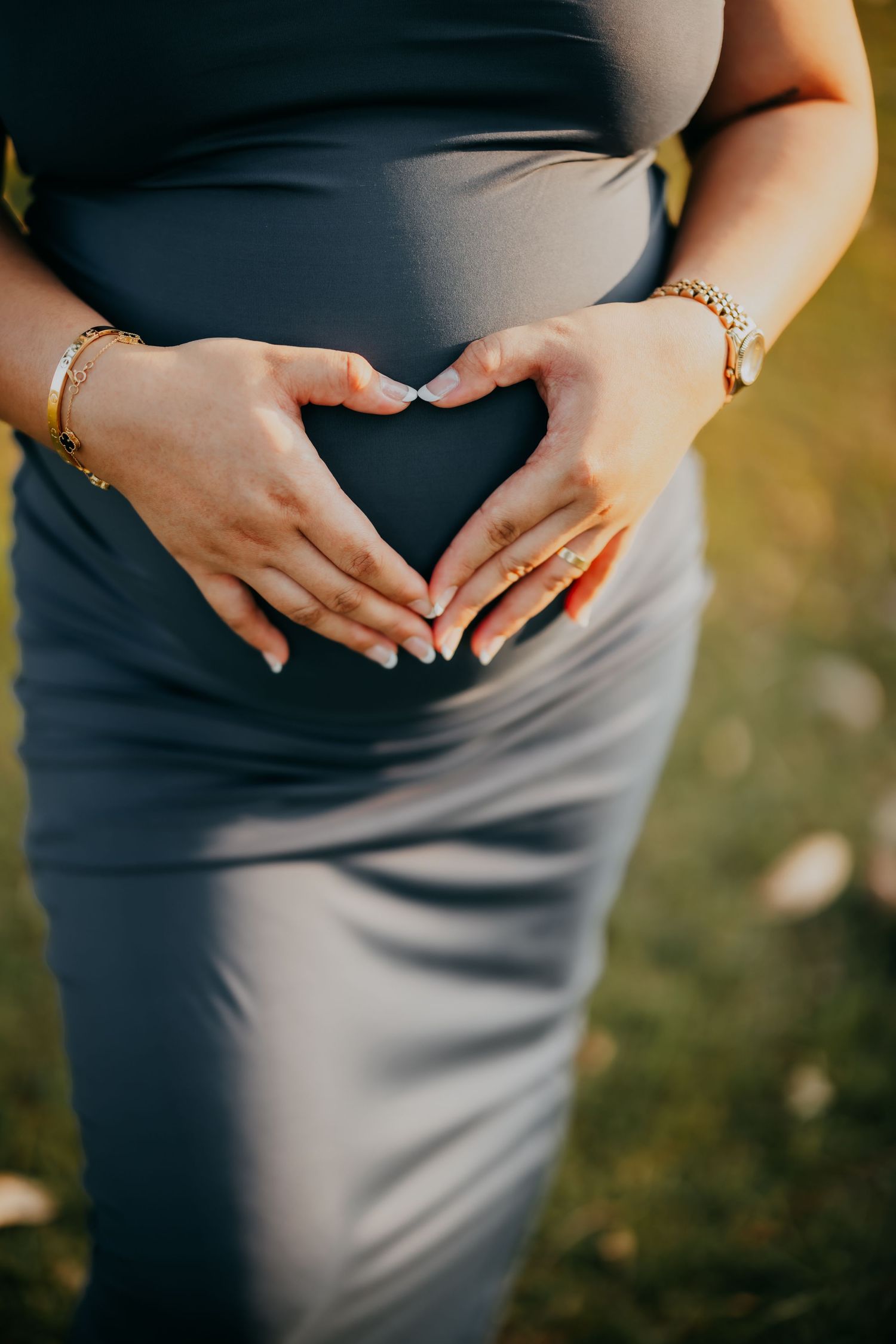Pregnant woman in grey dress forming a heart shape with her hands on her baby bump.