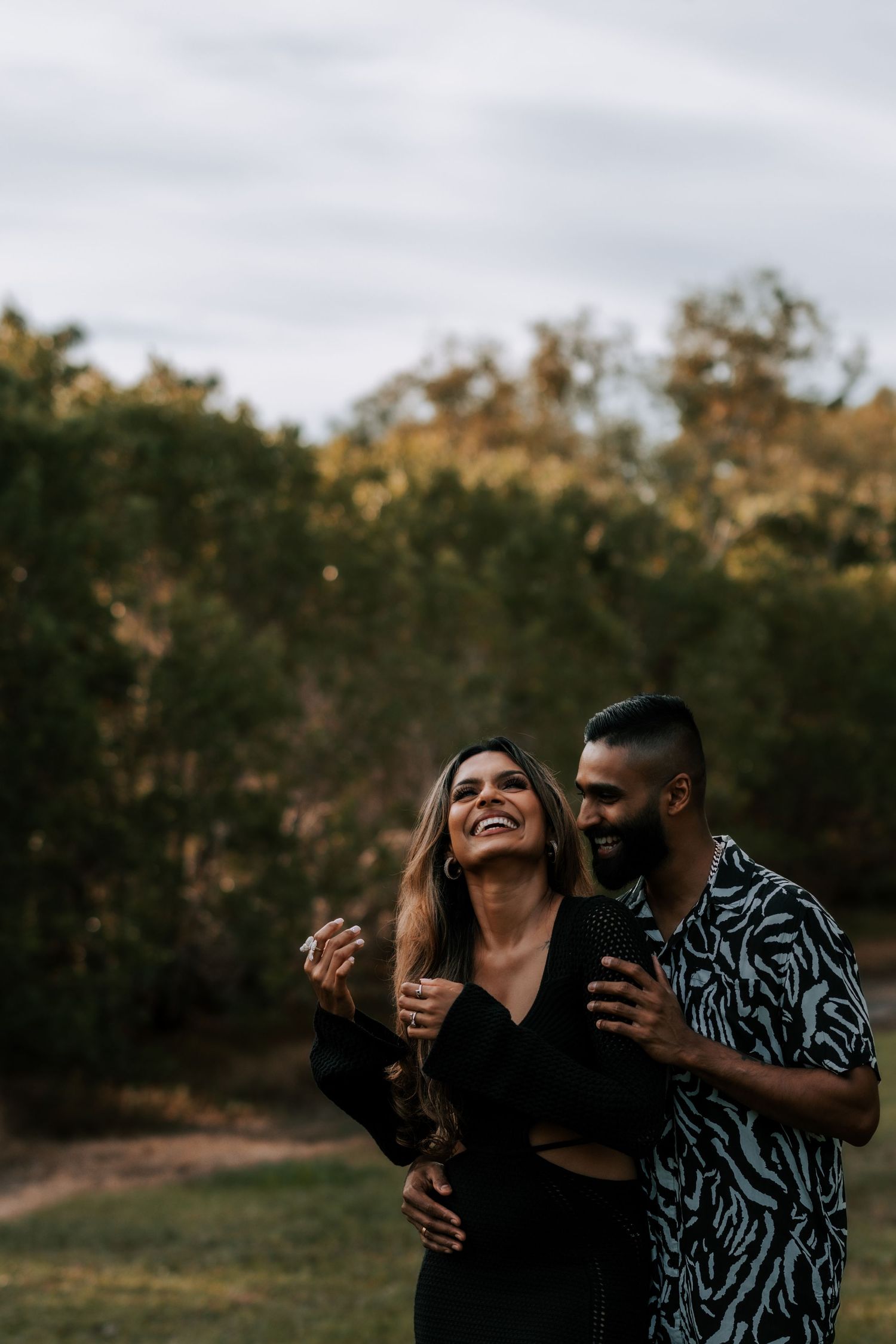 A happy couple embraces outdoors, laughing together in a natural park setting.