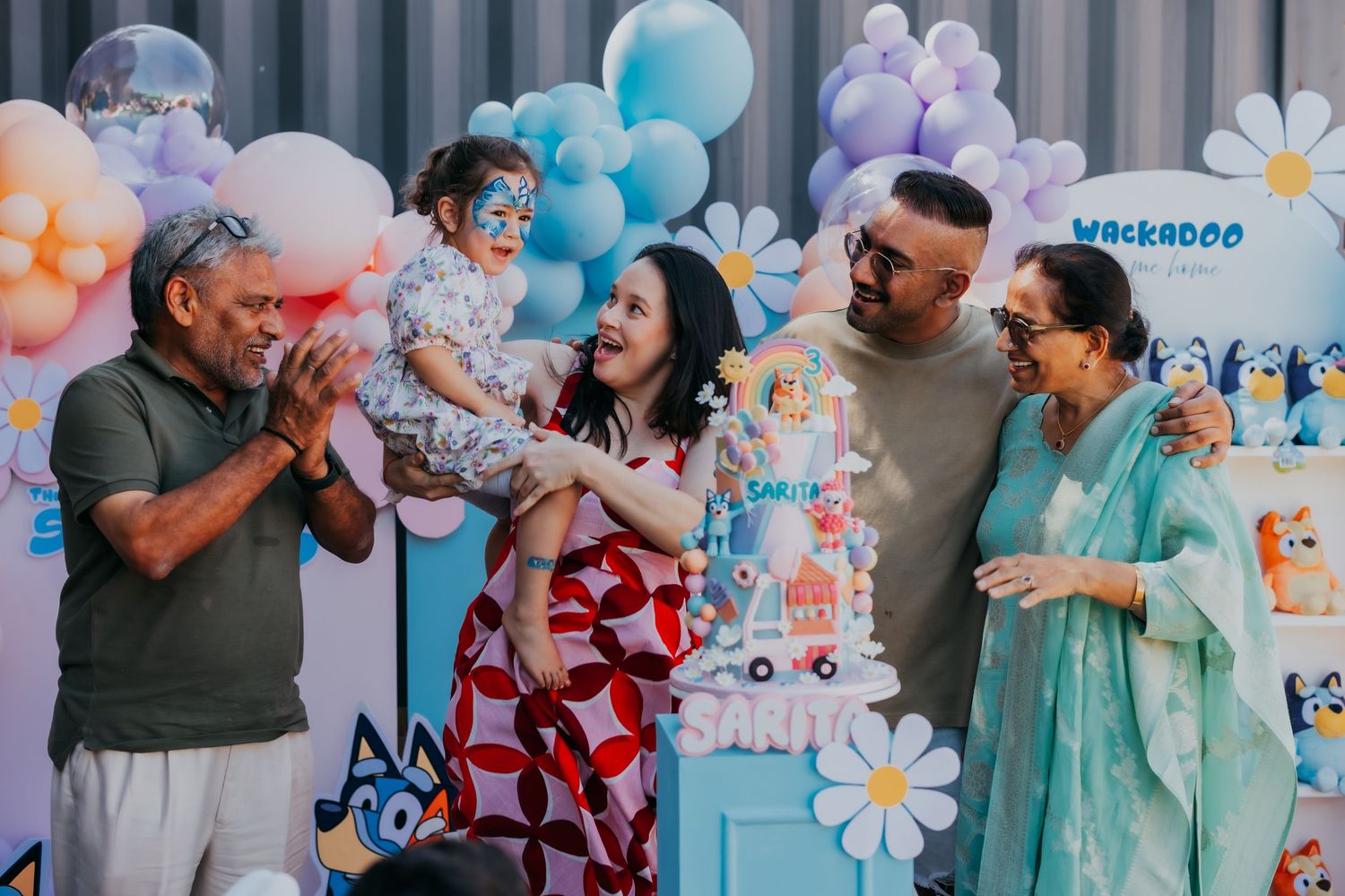 Family celebrating a baby's first birthday party with colorful balloon decorations and a themed cake.