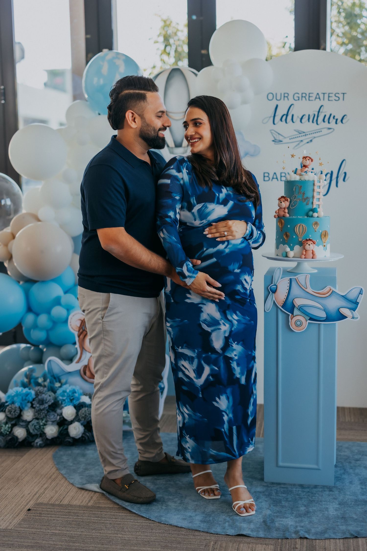 Couple at a baby shower posing in front of Our Greatest Adventure blue balloon backdrop.