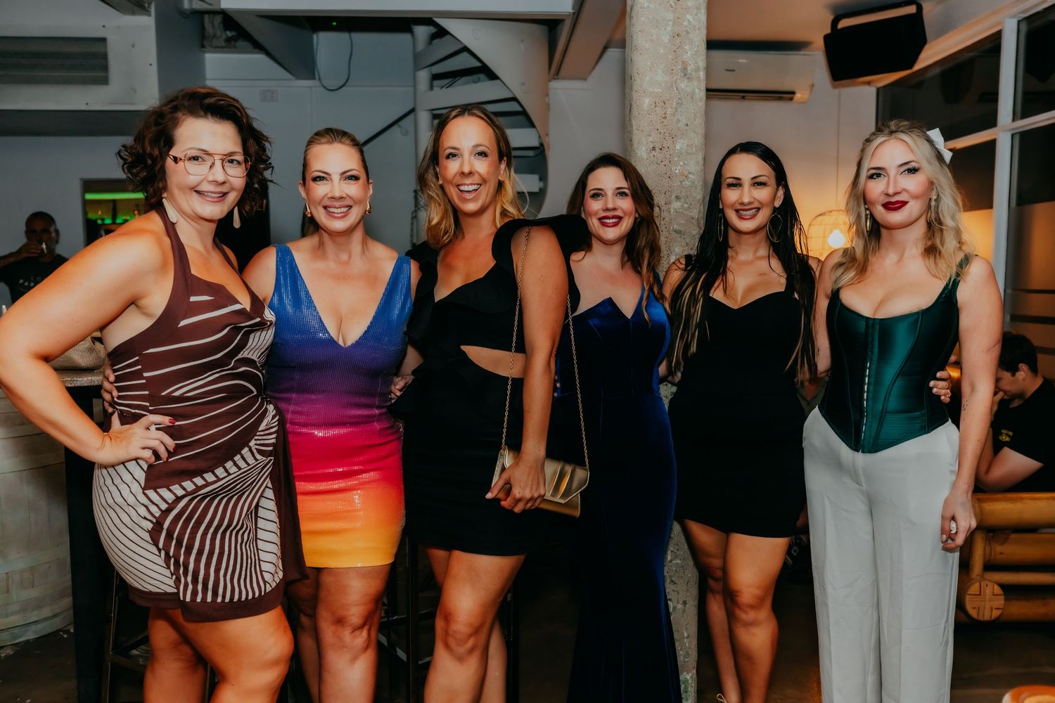 Six women pose together at an elegant evening party event.