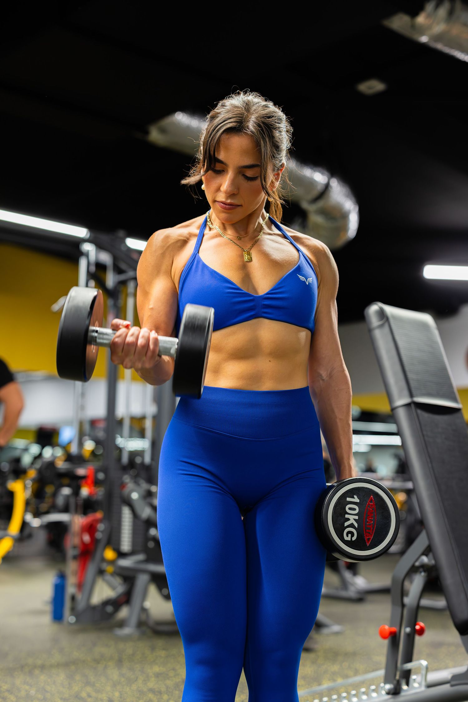 Fit woman in blue workout set doing dumbbell curls at the gym.