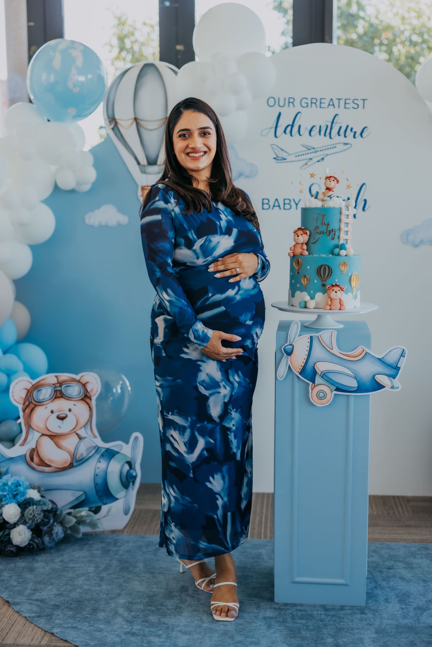 Pregnant woman in blue dress posing beside adventure themed baby shower cake.
