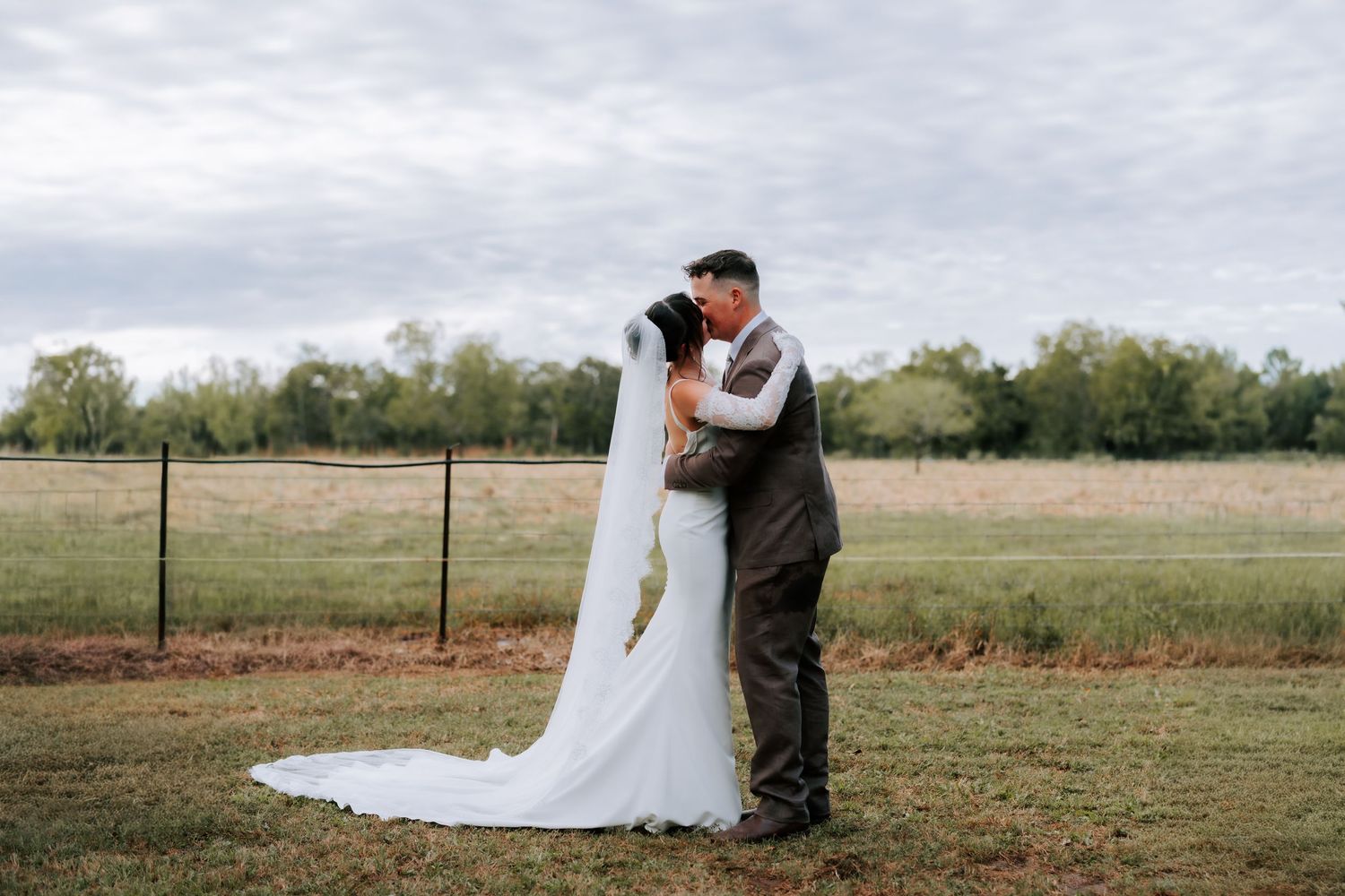 Bride and groom sharing a kiss in an open field at their rustic outdoor wedding.
