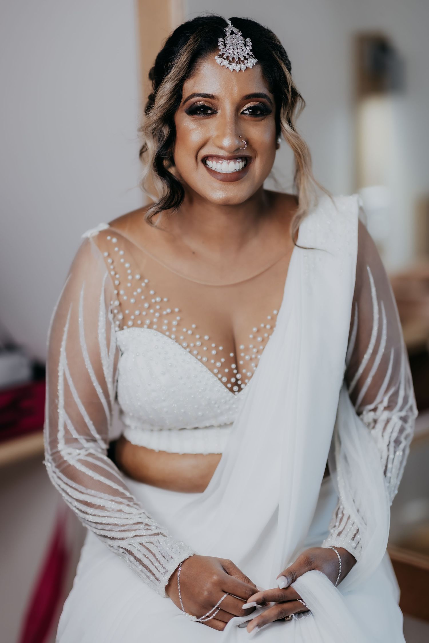 Radiant bride in white beaded saree with maang tikka smiling on wedding day.