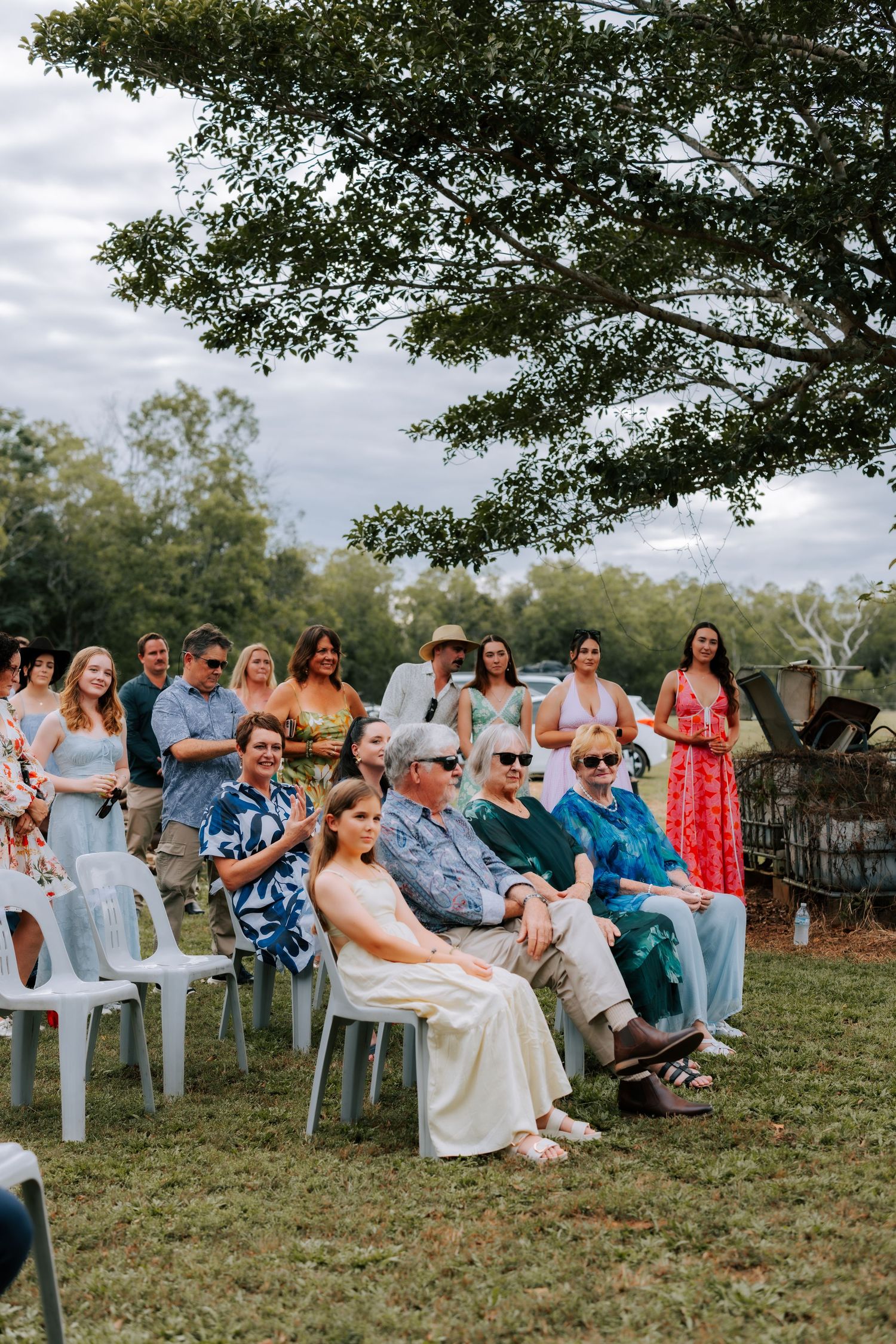 Guests seated outdoors at a rustic farm wedding ceremony under cloudy skies.