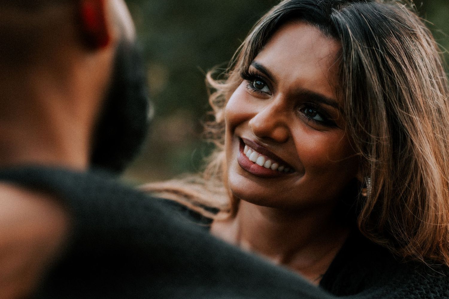A woman smiles joyfully at her partner during a romantic outdoor couples photo session.