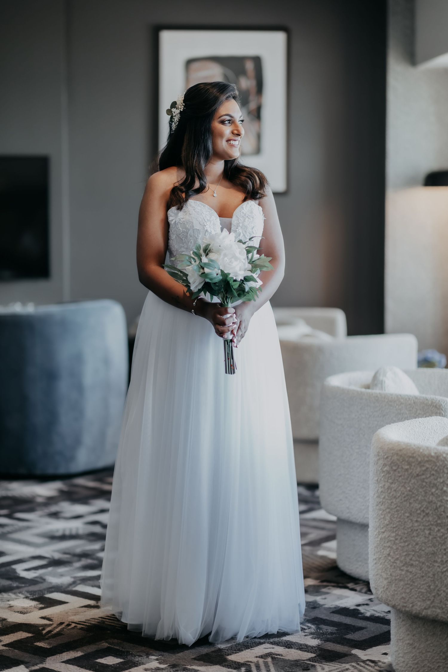 Beautiful bride in a white tulle ball gown holding a white bouquet in a modern hotel suite.