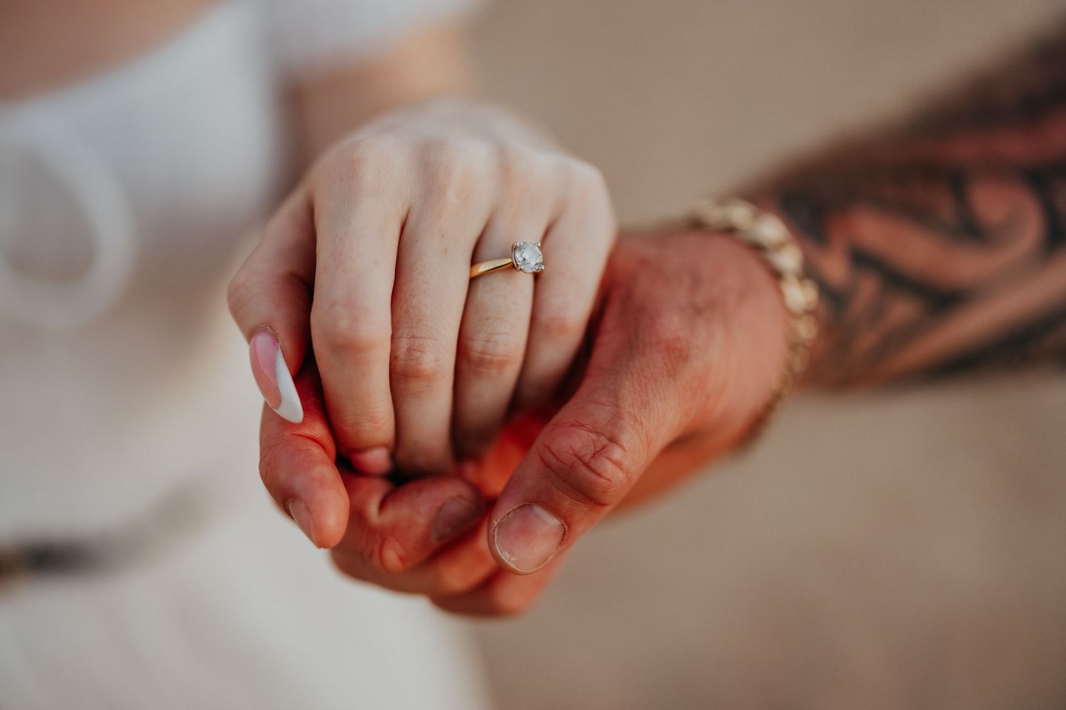 Close-up of an engagement ring on a woman's hand held by a tattooed man.