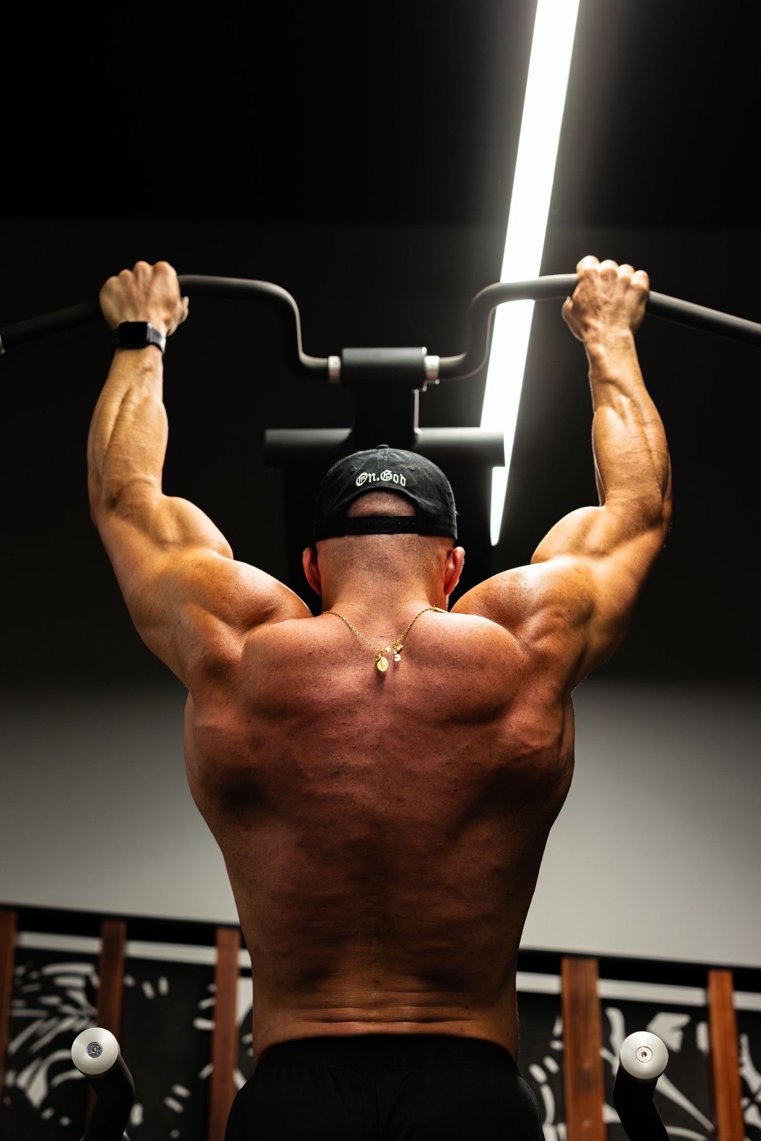 Muscular man performing wide-grip lat pulldown exercise on a cable machine in a gym.