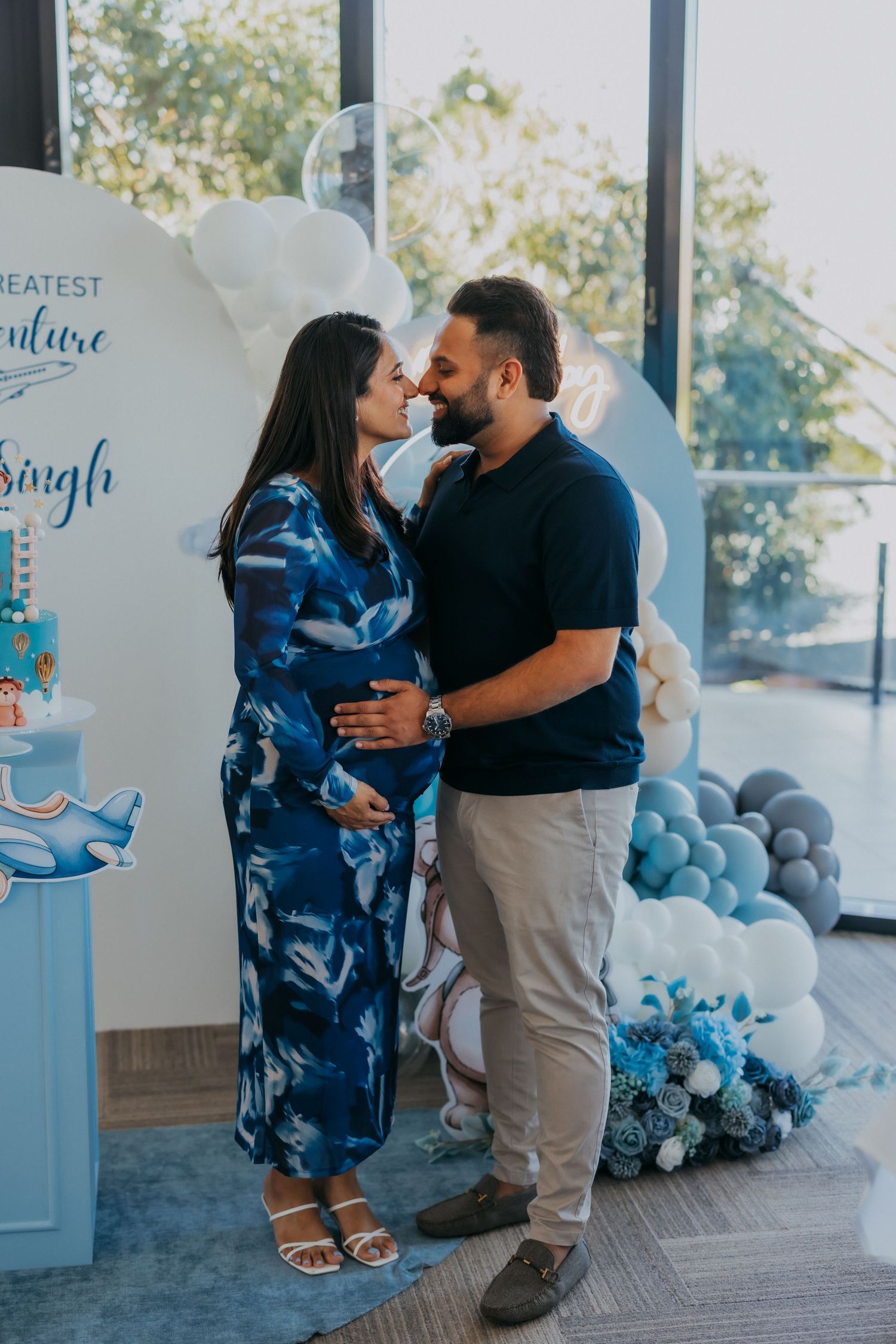 Expecting couple sharing tender moment at blue adventure themed baby shower setup.