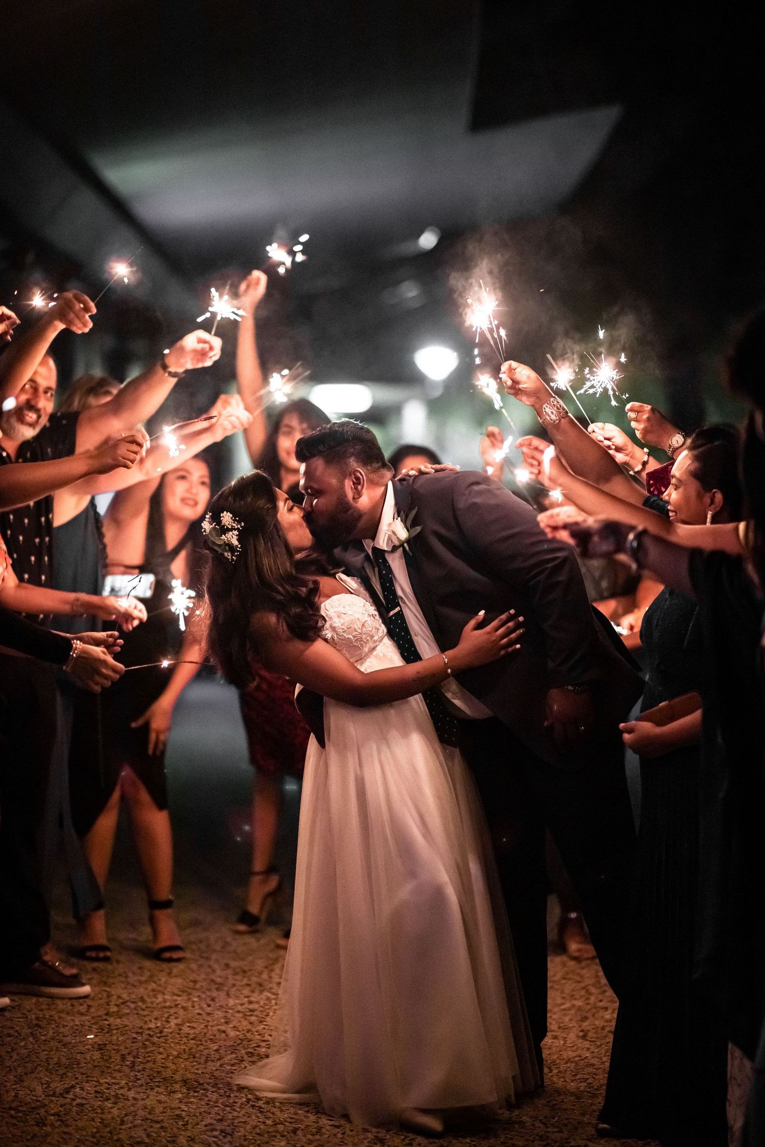 Newlyweds share a romantic kiss surrounded by guests holding sparklers during wedding send-off.