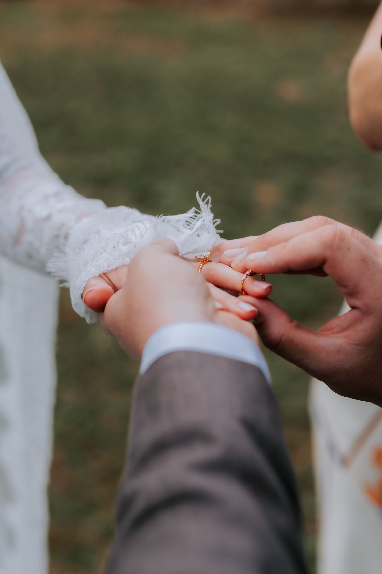Groom placing a gold wedding ring on brides finger during outdoor ceremony.