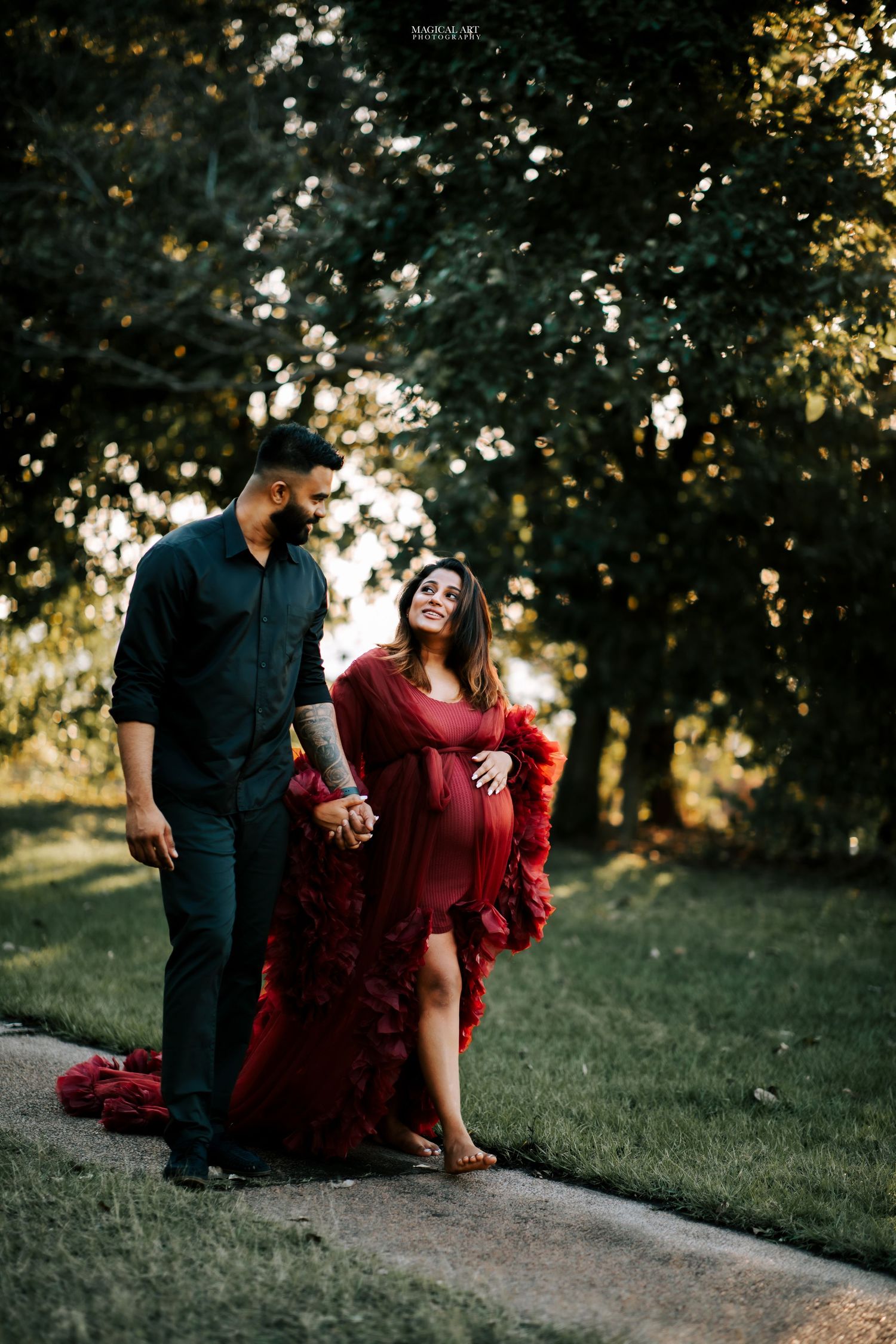 Couple walking in a park at golden hour, pregnant woman in flowing red maternity gown.