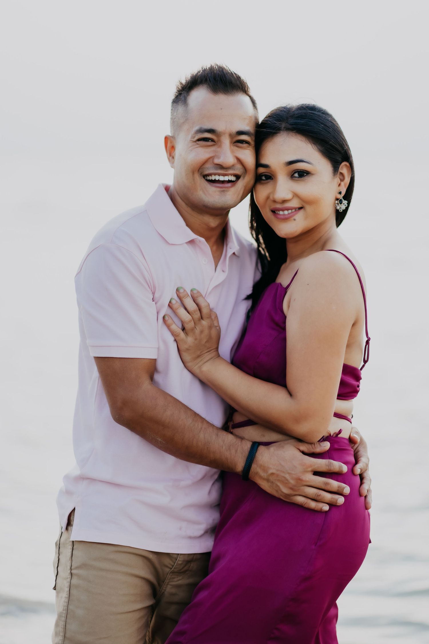 A laughing couple embraces warmly on a beach, with the woman in a vibrant purple dress.