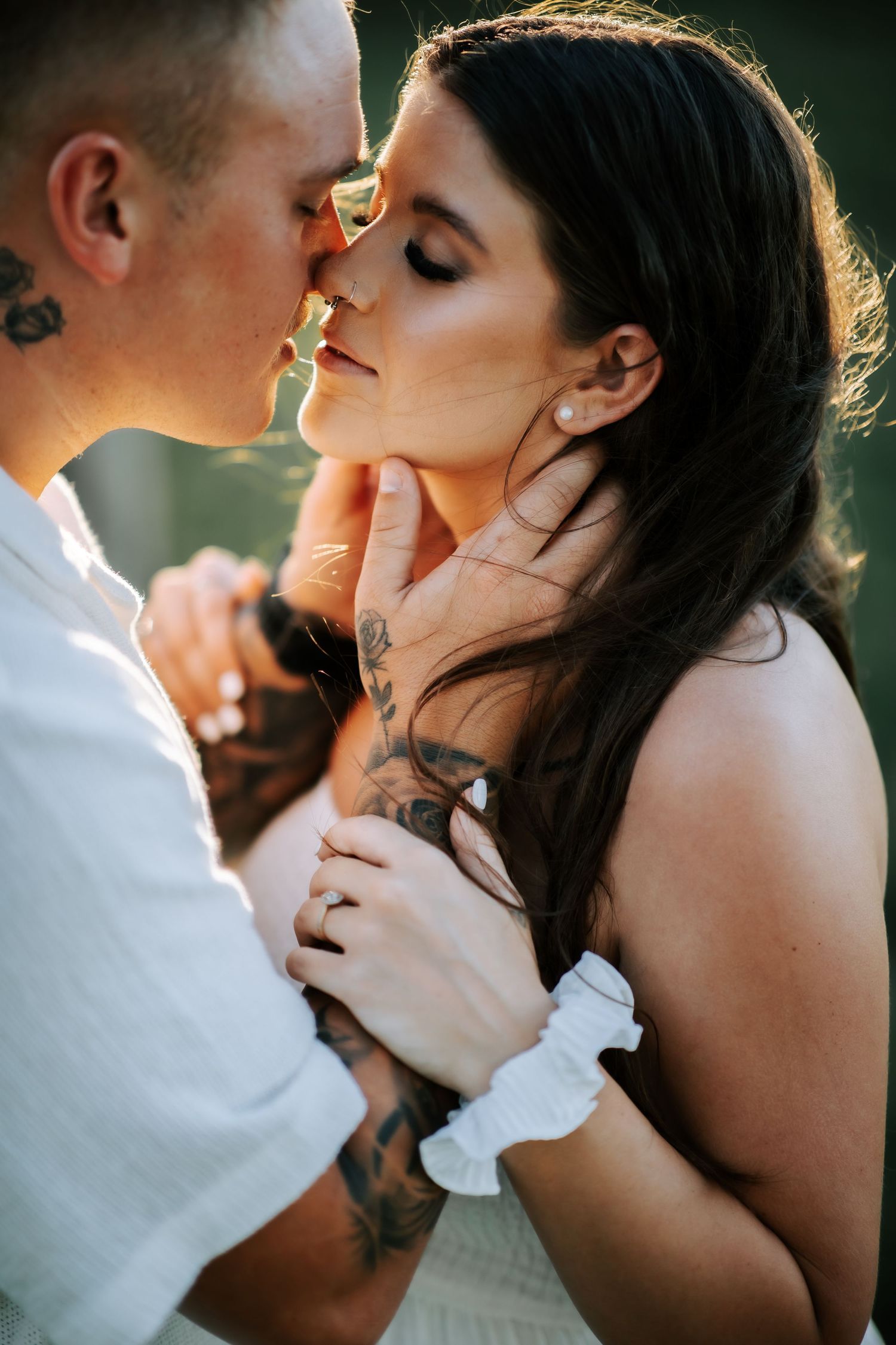 Tattooed couple sharing an intimate moment, almost kissing, in warm golden sunset light.