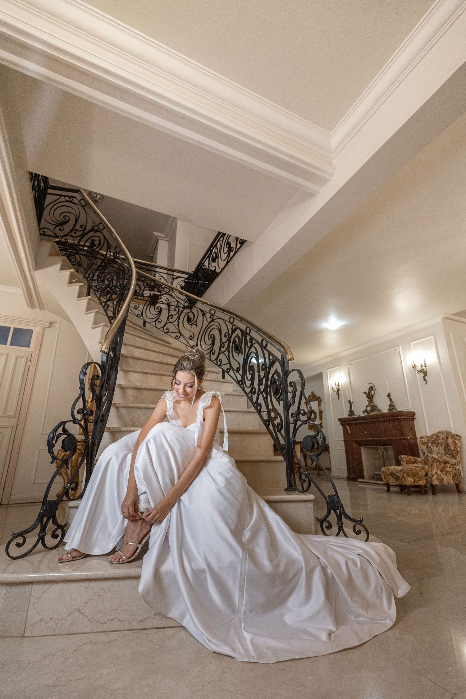 Elegant bridal portrait on grand staircase with ornate iron railings in white interior.