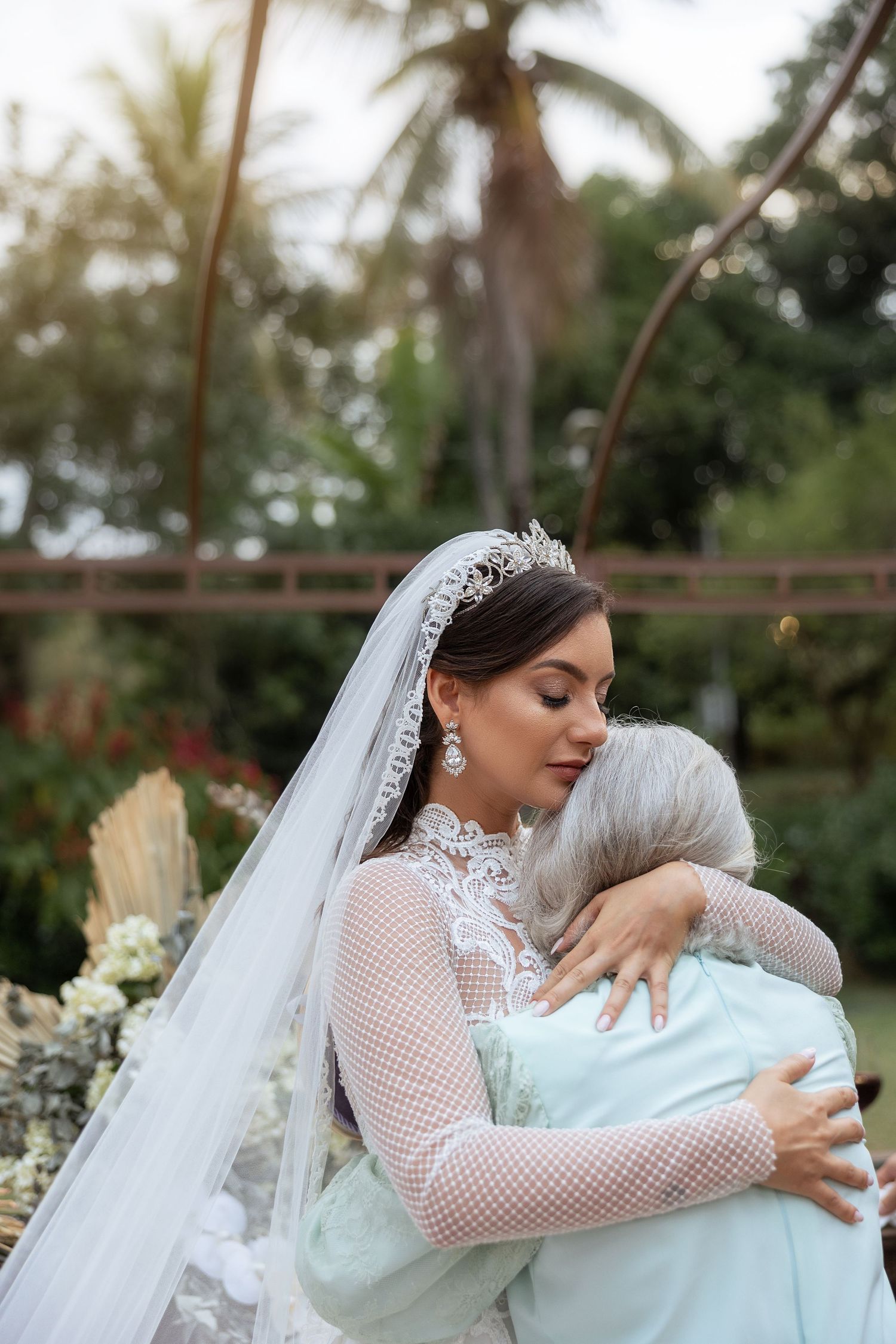 Emotional embrace between bride and elderly relative at outdoor wedding.