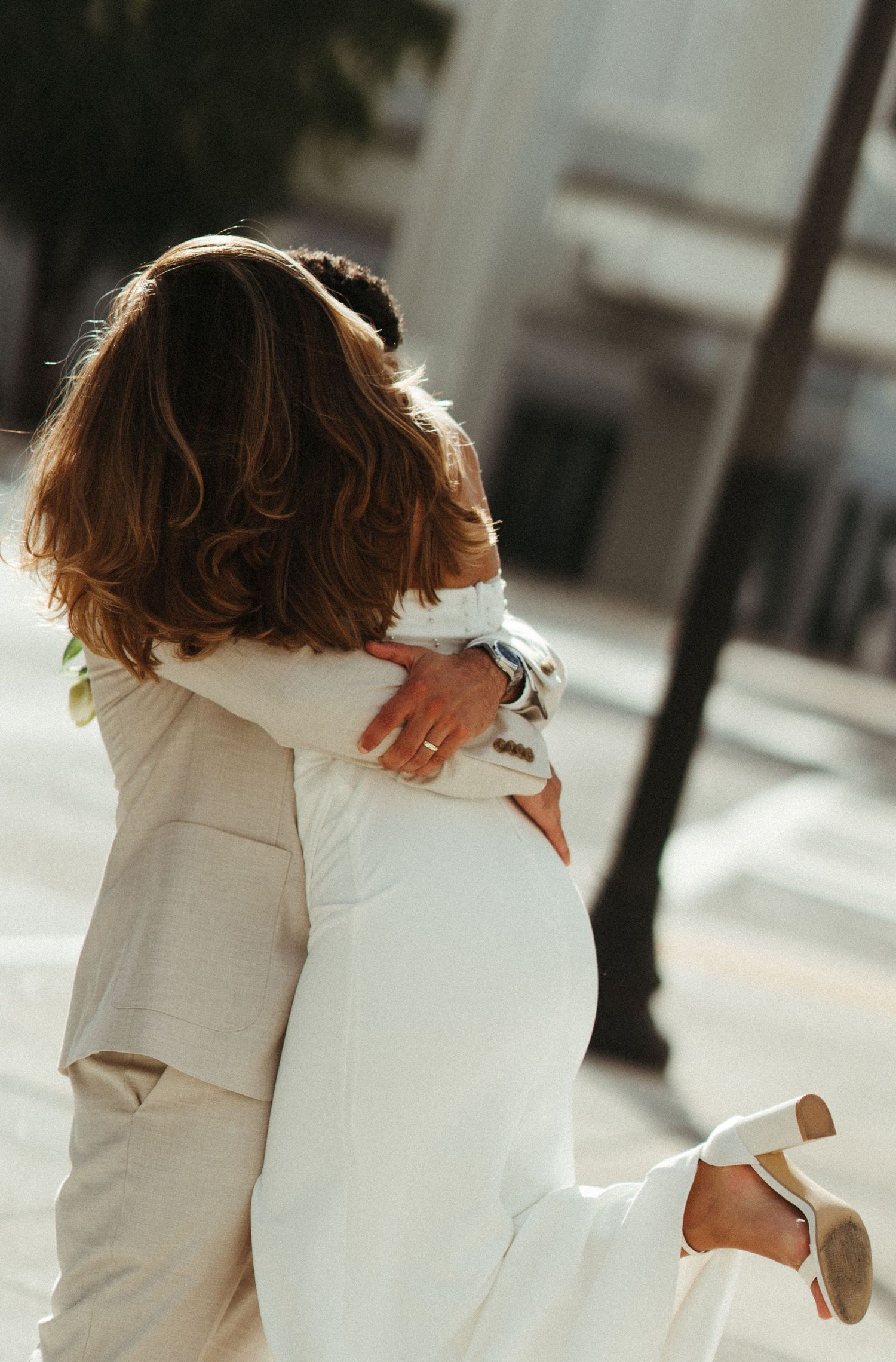 A couple wearing white embraces and spins together in a romantic dance sequence on a sunny day.