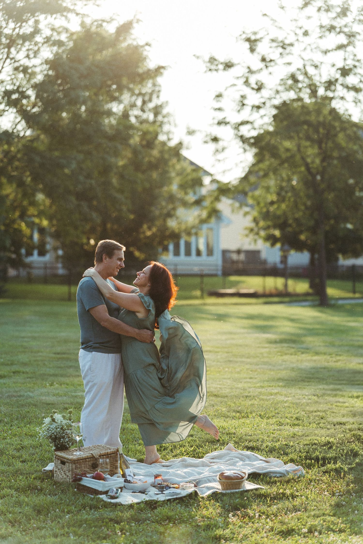 Couple enjoying romantic sunset picnic on blanket in grassy field.
