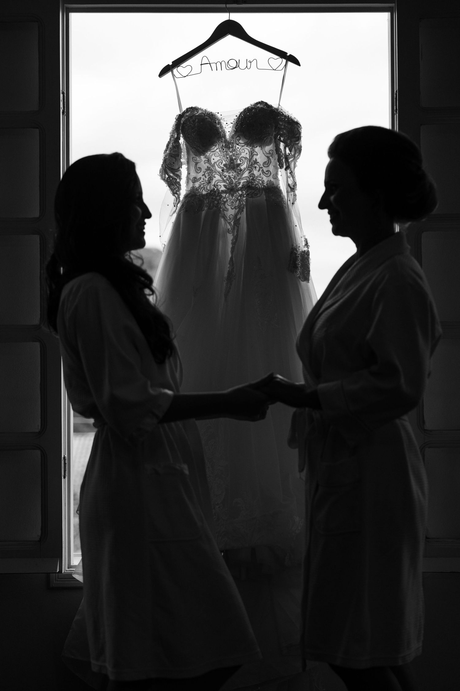 Silhouetted figures prepare wedding attire in a backlit room creating dramatic shadows.