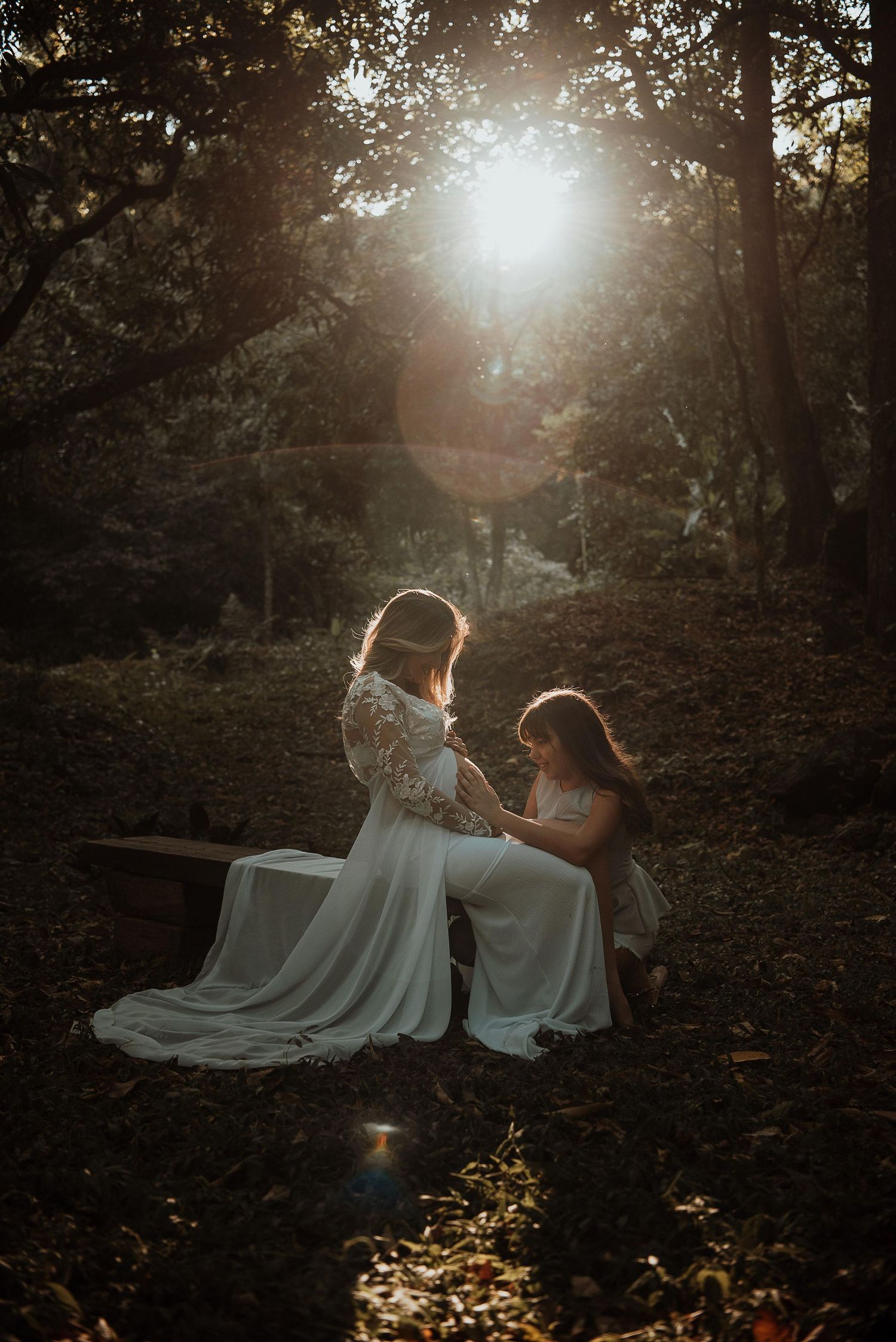 Ethereal forest photoshoot with white dresses and golden sunlight filtering through trees.