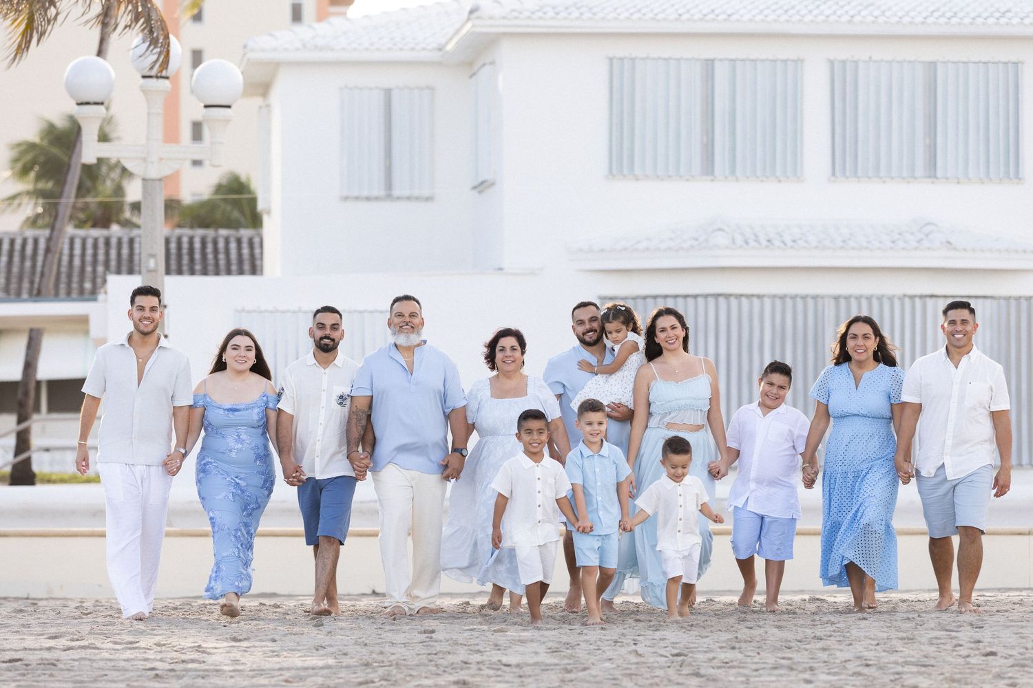 Group wearing coordinated white and light blue outfits walking together on beach during family photo session.