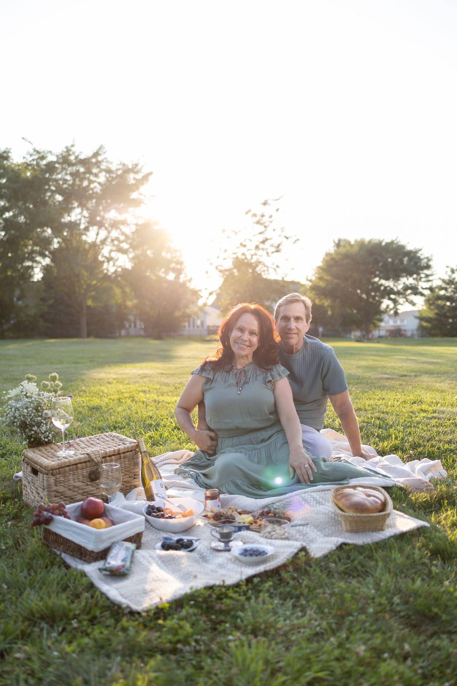 Couple relaxing on picnic blanket with spread of food during golden hour.