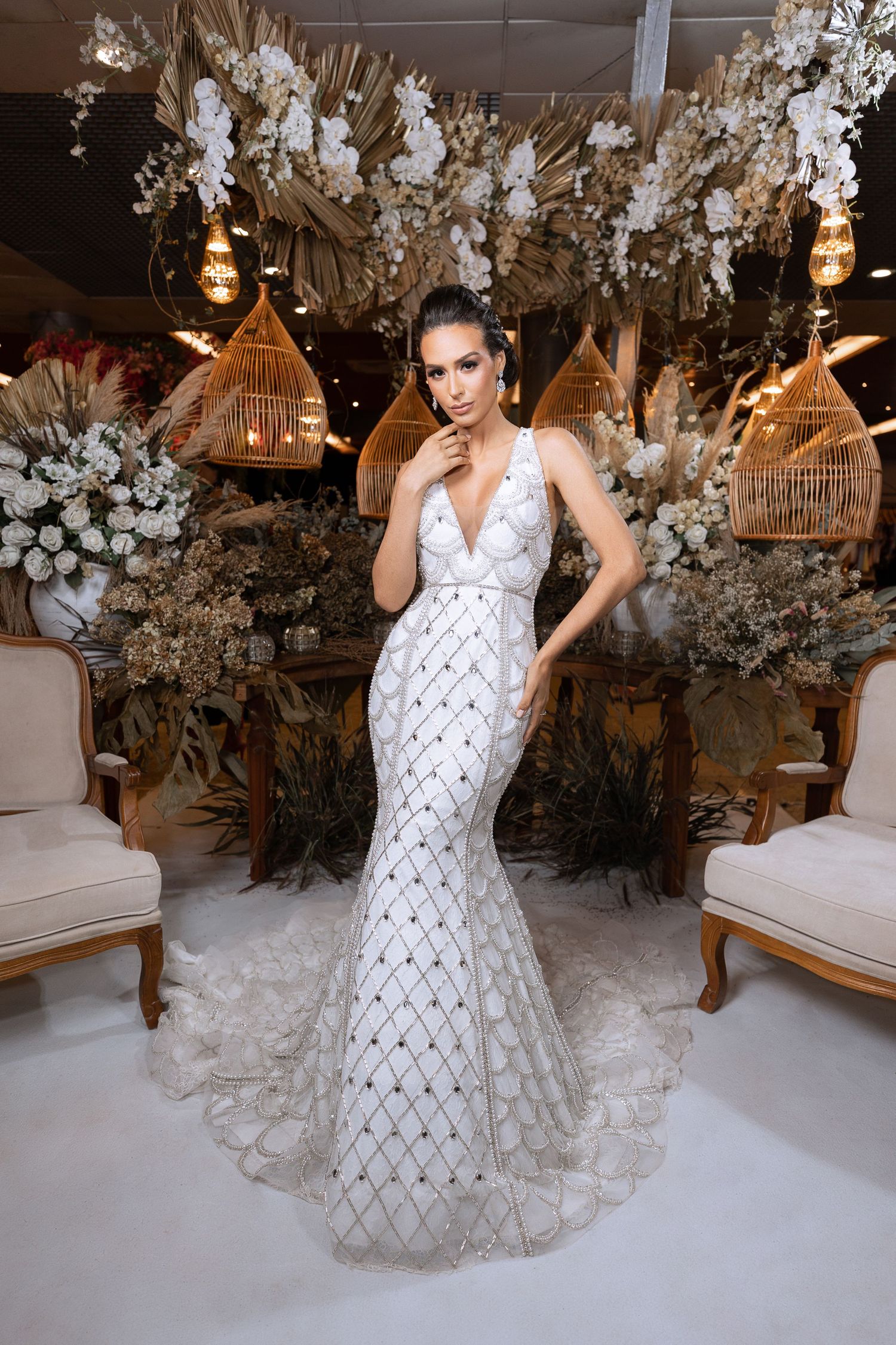 A bride in an elegant white geometric pattern dress poses in a room decorated with hanging flowers.