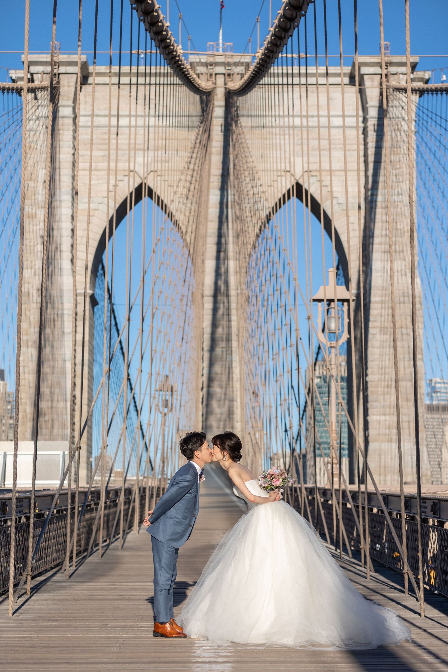 Wedding couple sharing intimate moment on Brooklyn Bridge with flowing white dress.