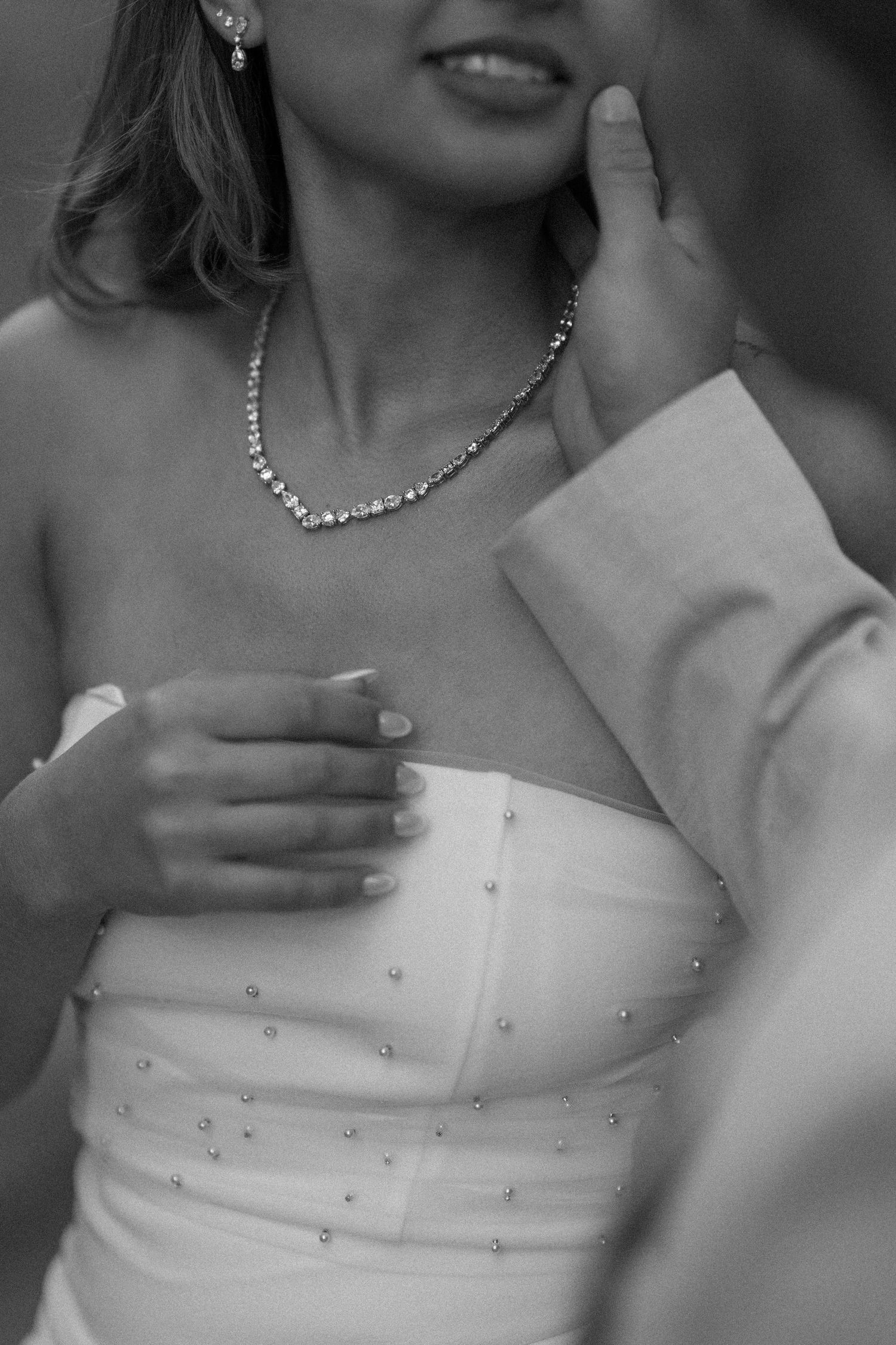 A black and white close-up shows a white strapless wedding dress with delicate crystal embellishments.