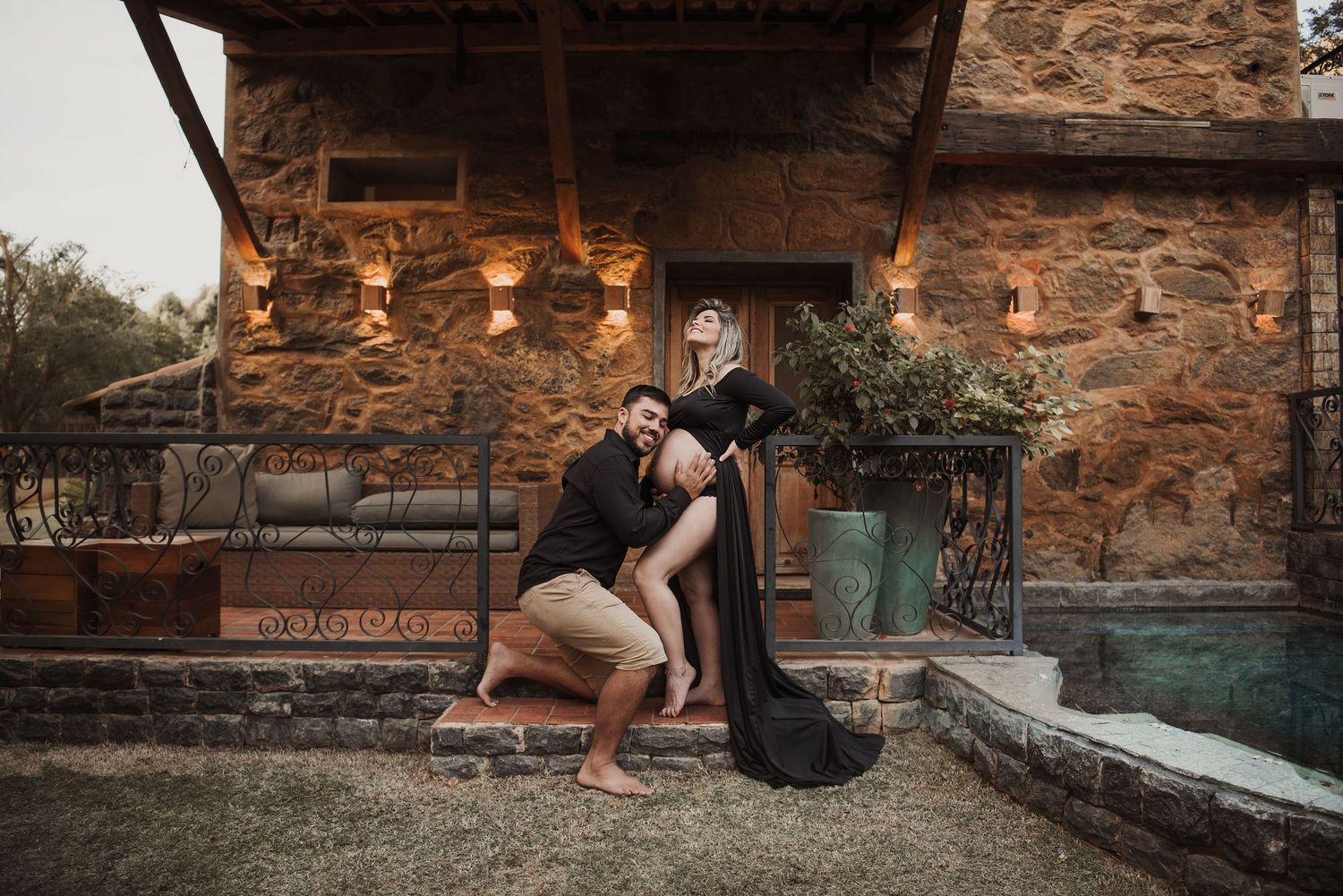 Couple in formal attire poses together against rustic stone walls during sunset photoshoot.